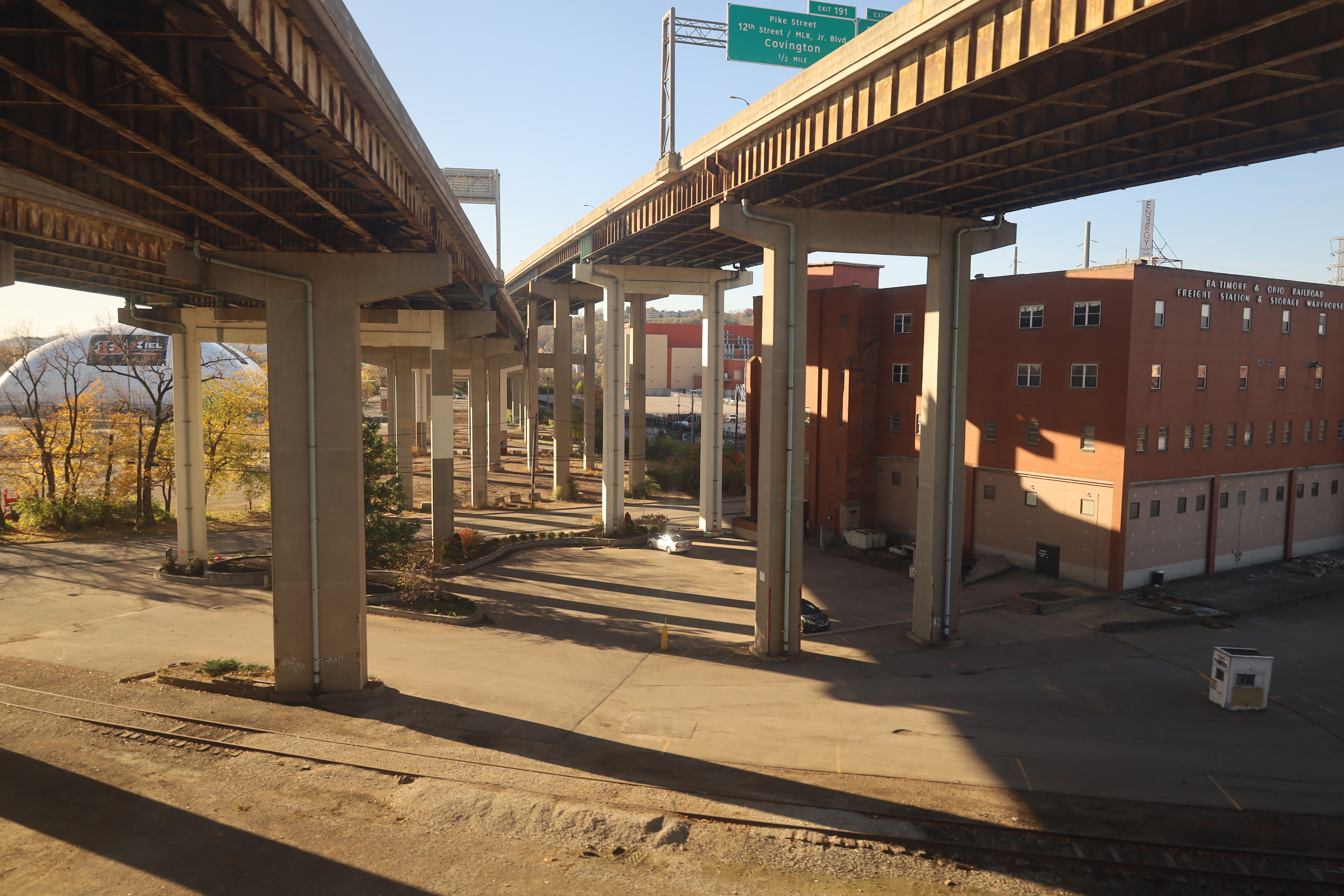 Concrete highway overpass columns above railroad tracks with a brick building in the background.