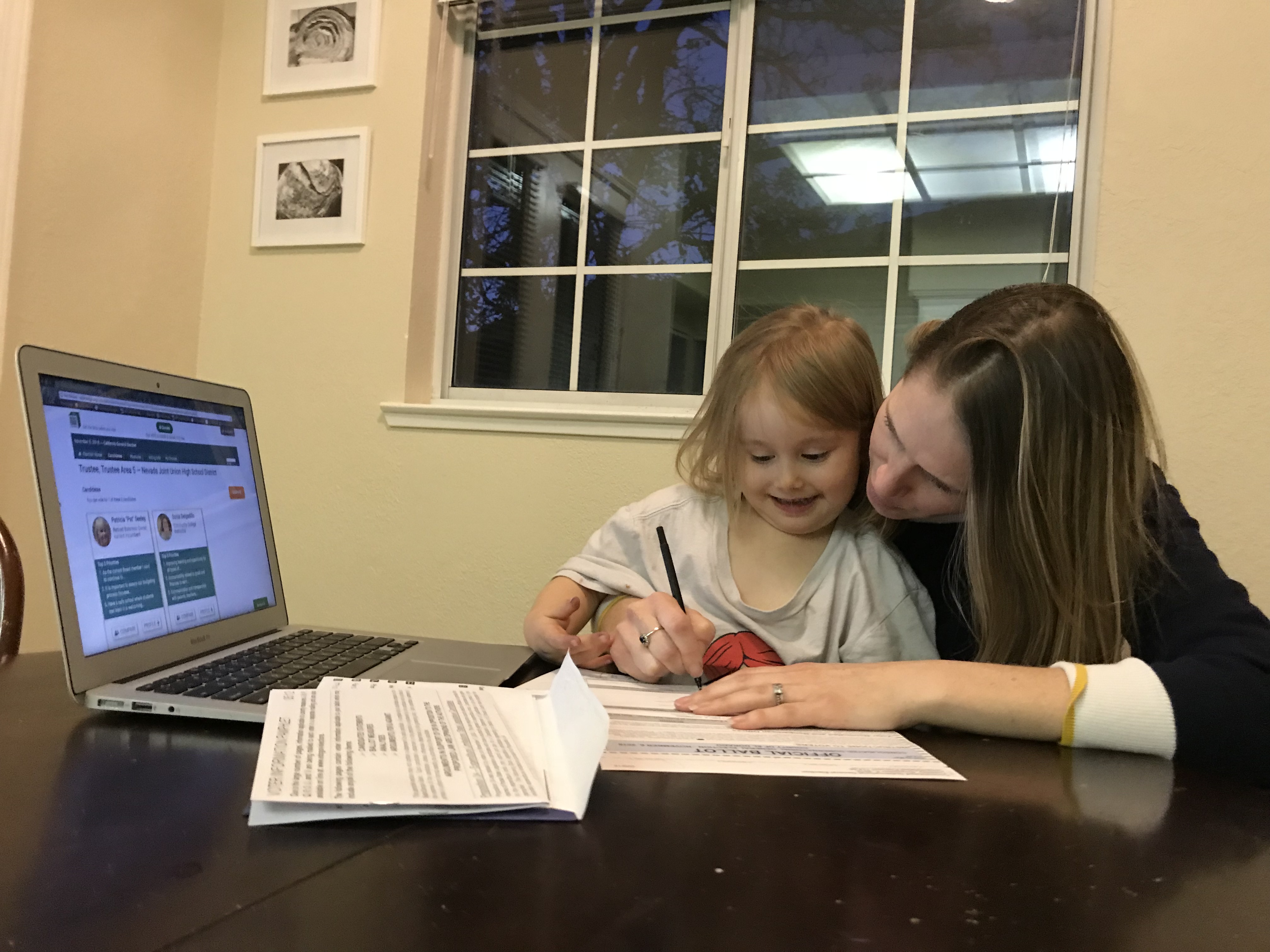 Woman and child sit at a table with a laptop open to a voter information website.