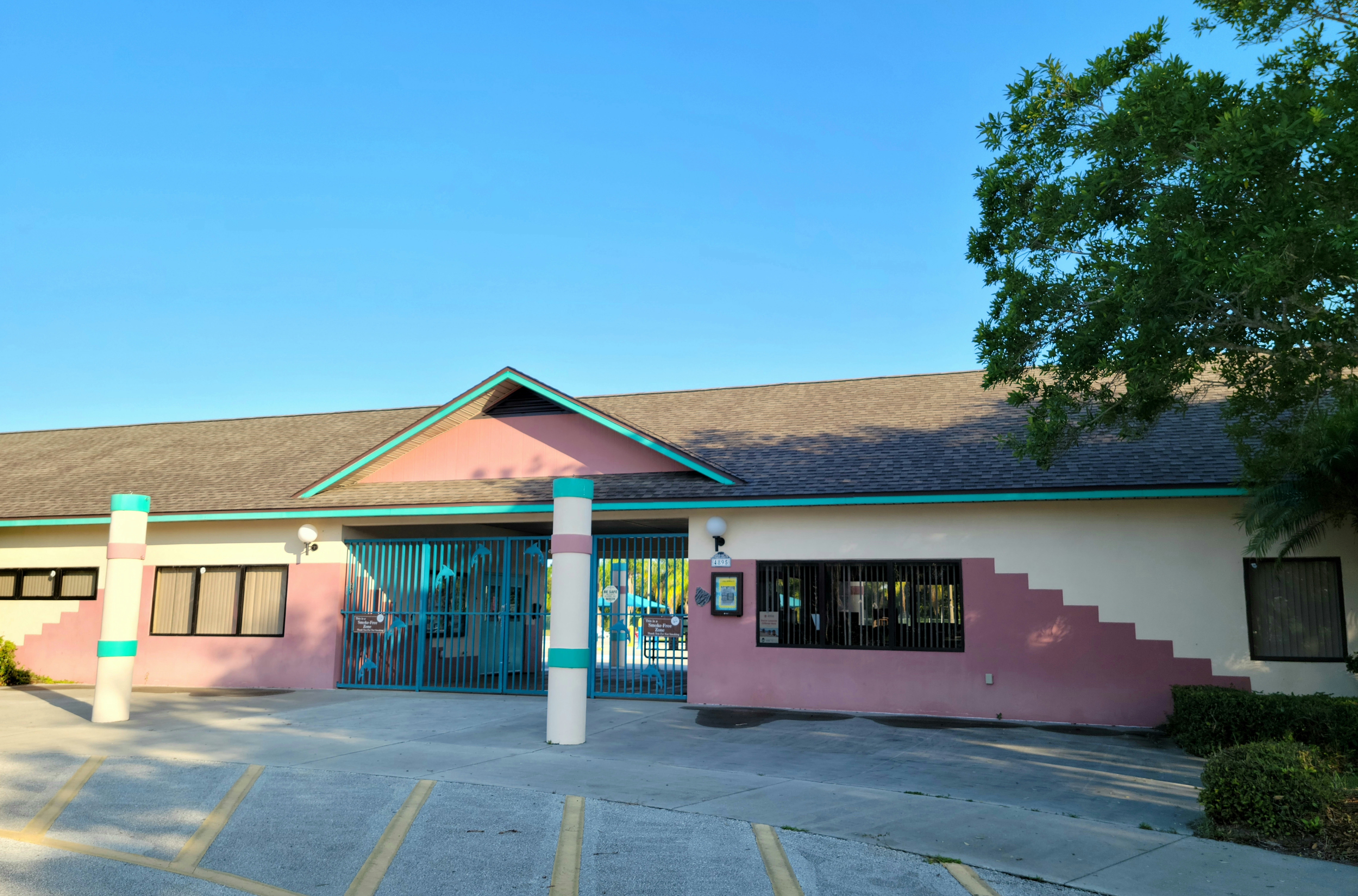 Exterior of a public aquatic center building with a gated entrance and parking lot.