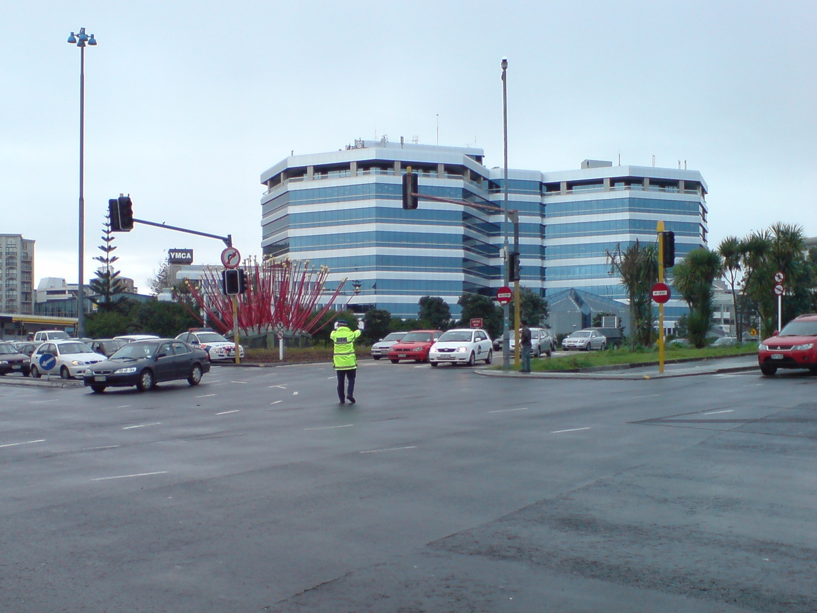 Officer in yellow vest standing in intersection directing vehicle traffic by hand.