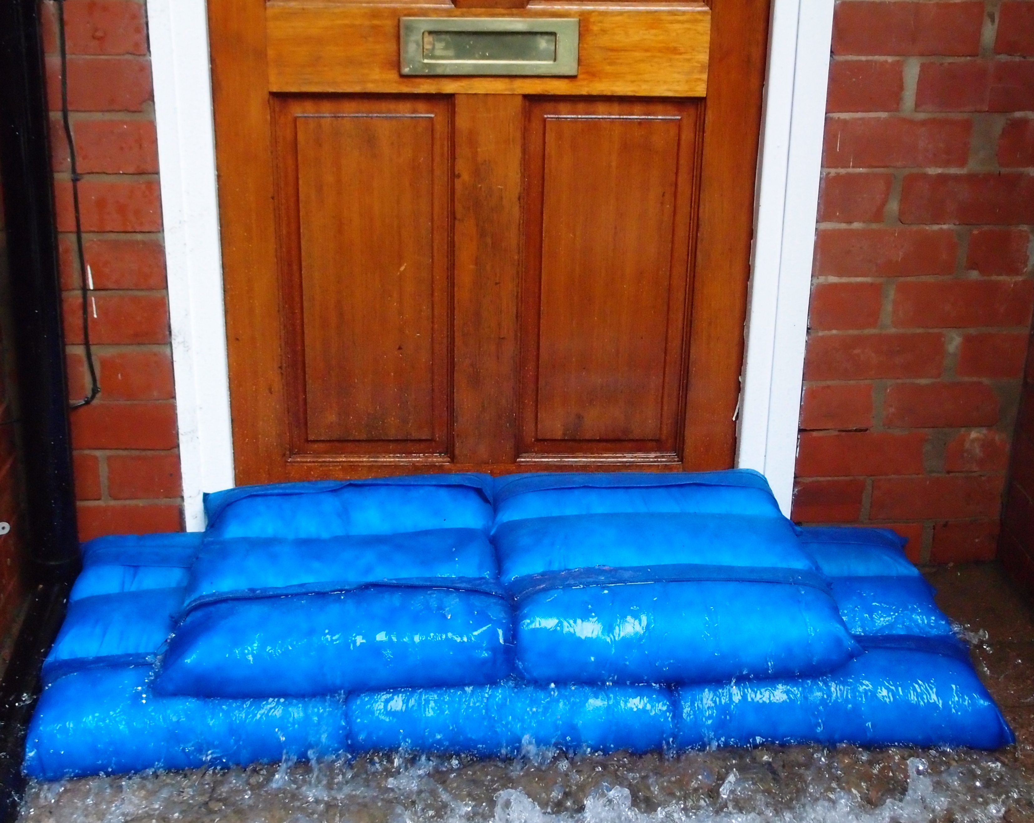 Blue sandbags stacked in two rows against a wooden front door.