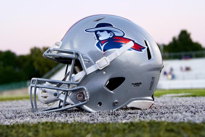 Silver football helmet with a pioneer mascot logo resting on a grass field.