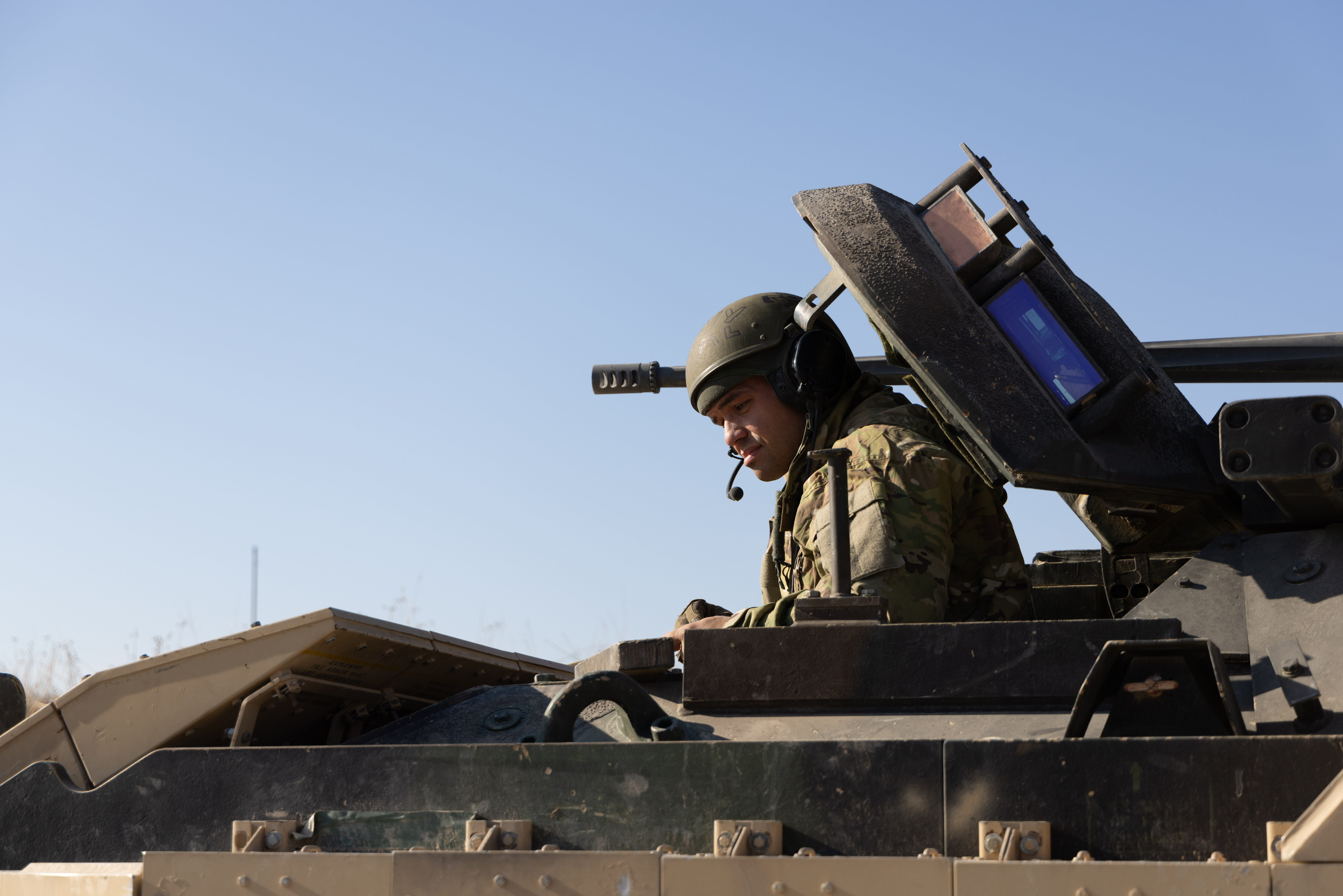 U.S. soldier in combat helmet seated in the open hatch of a Bradley Fighting Vehicle.