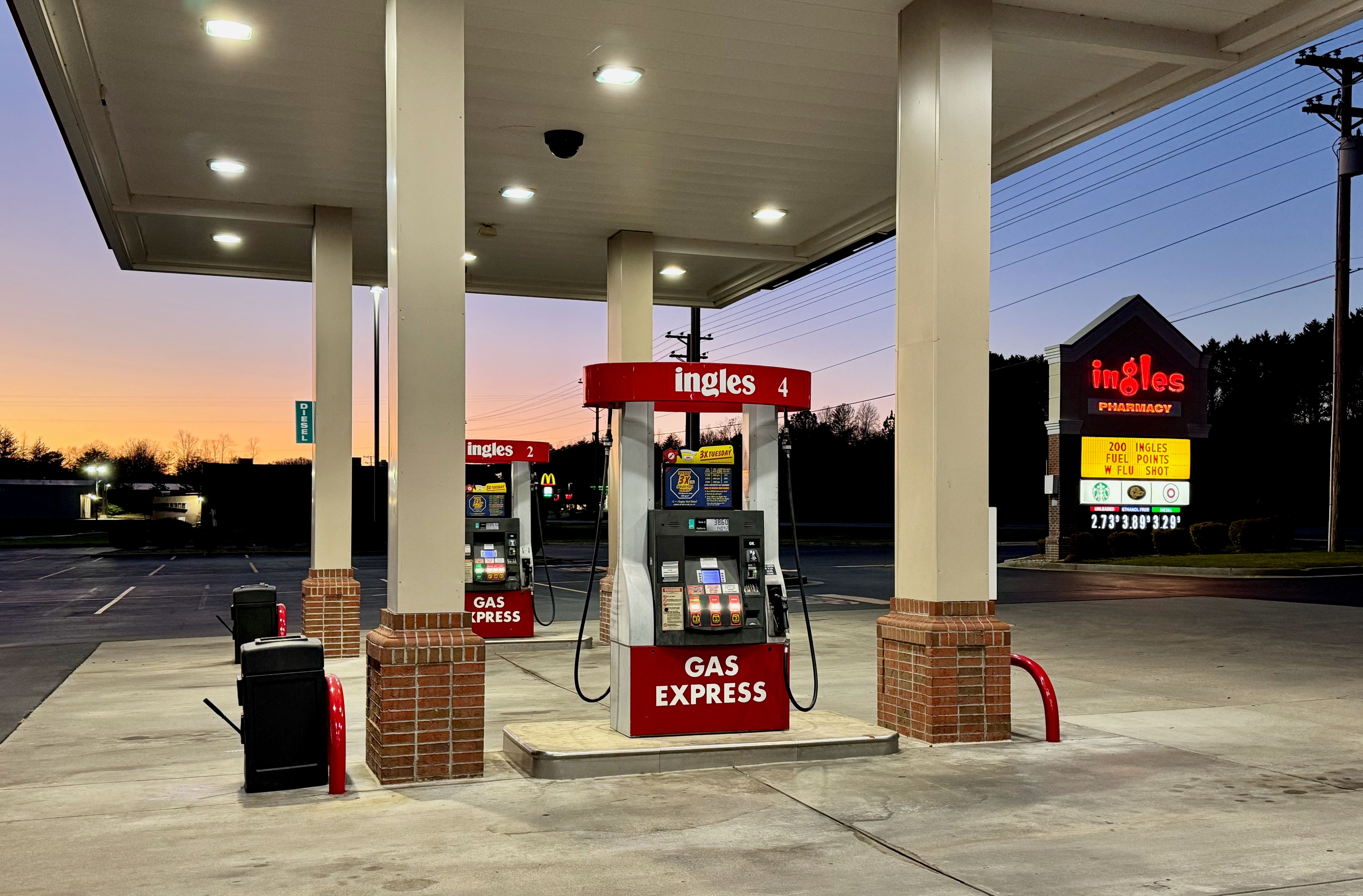 Fuel pumps under a canopy at a gas station at dusk.