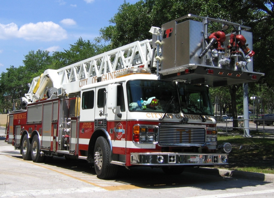 A red and white aerial ladder fire truck with tower and water cannon parked outdoors.