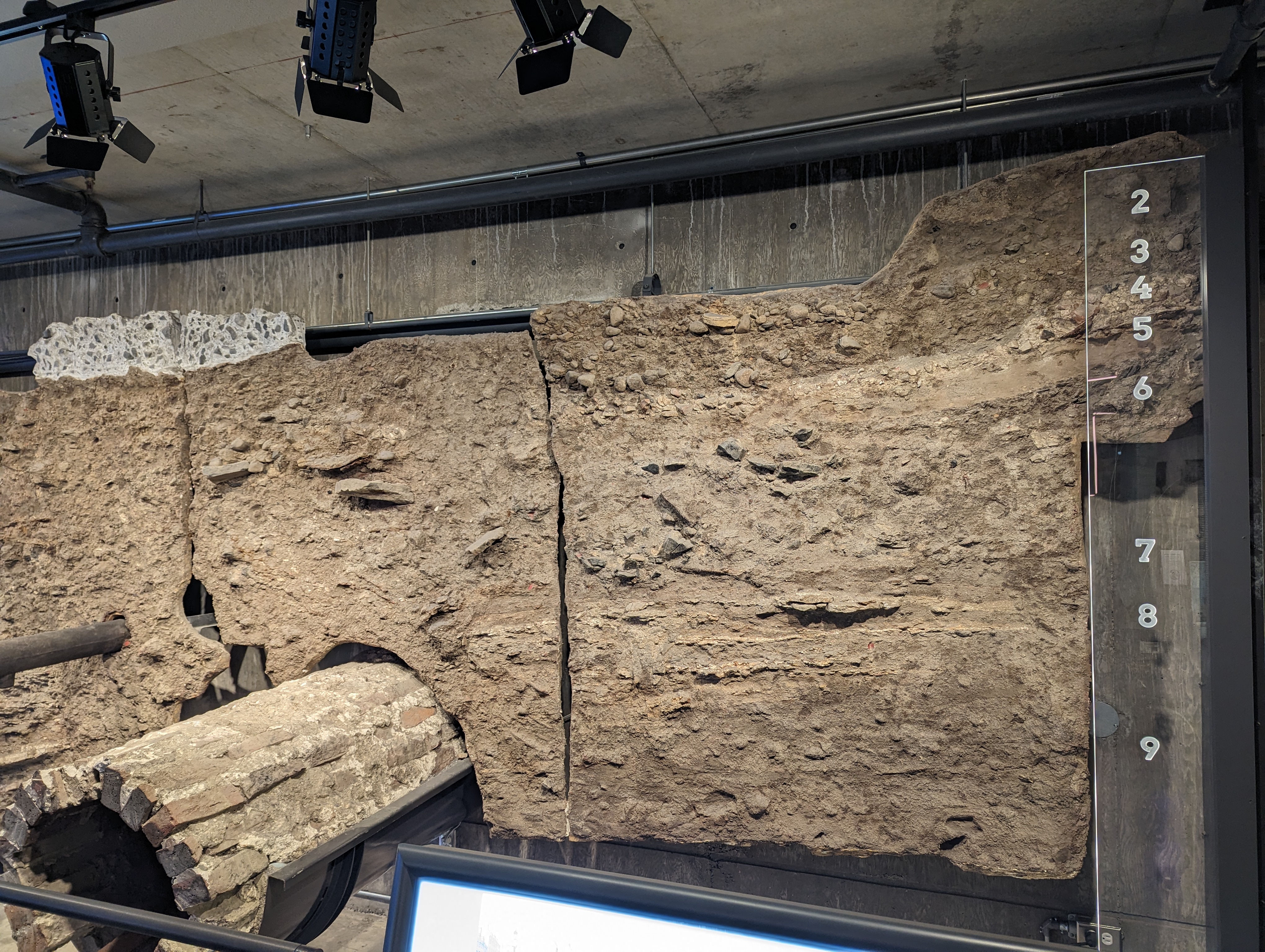 Museum display showing excavated soil layers with an old brick sewer pipe and cast iron water main.
