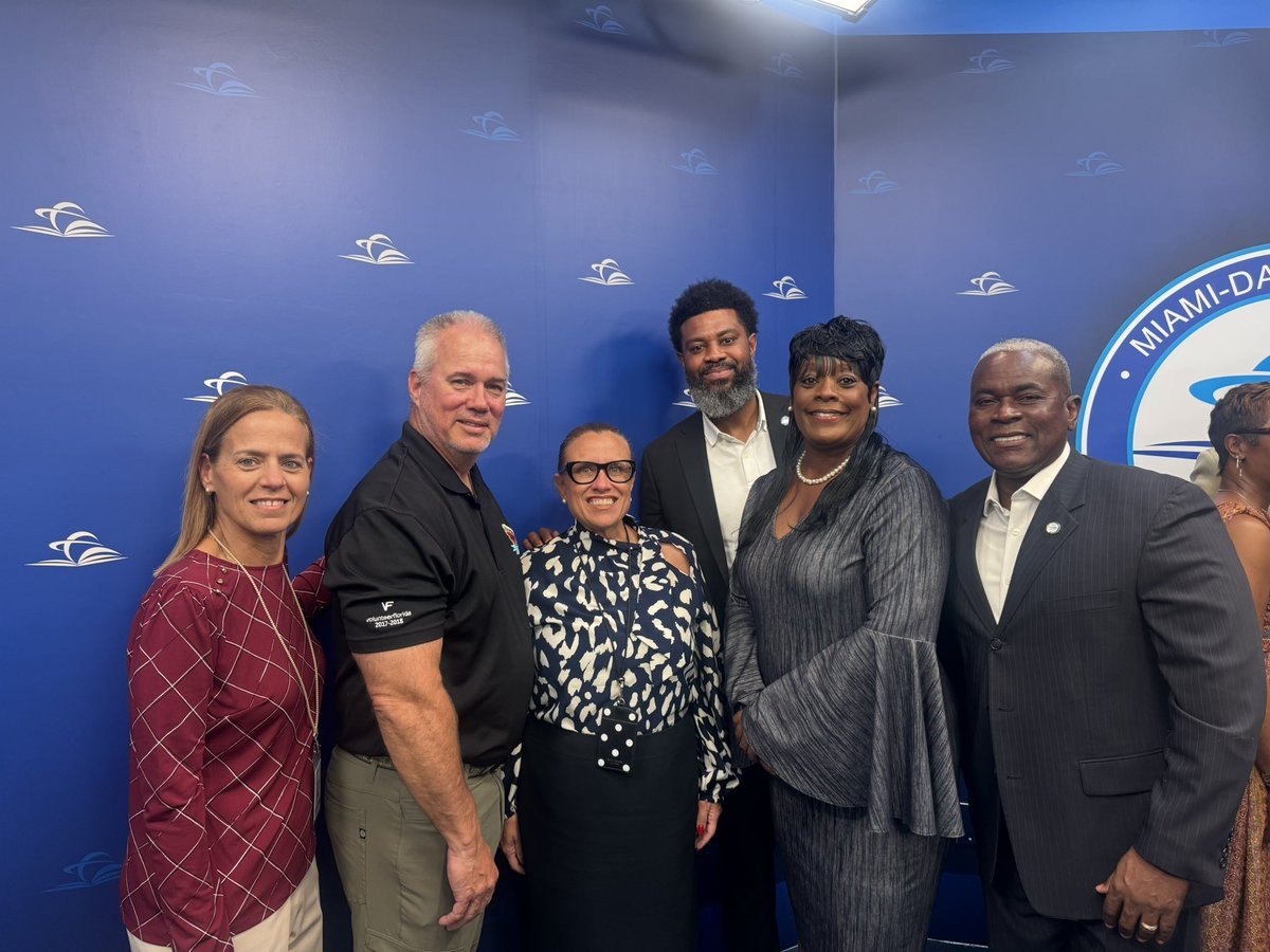 Six people posing together in front of a blue Miami-Dade County backdrop.