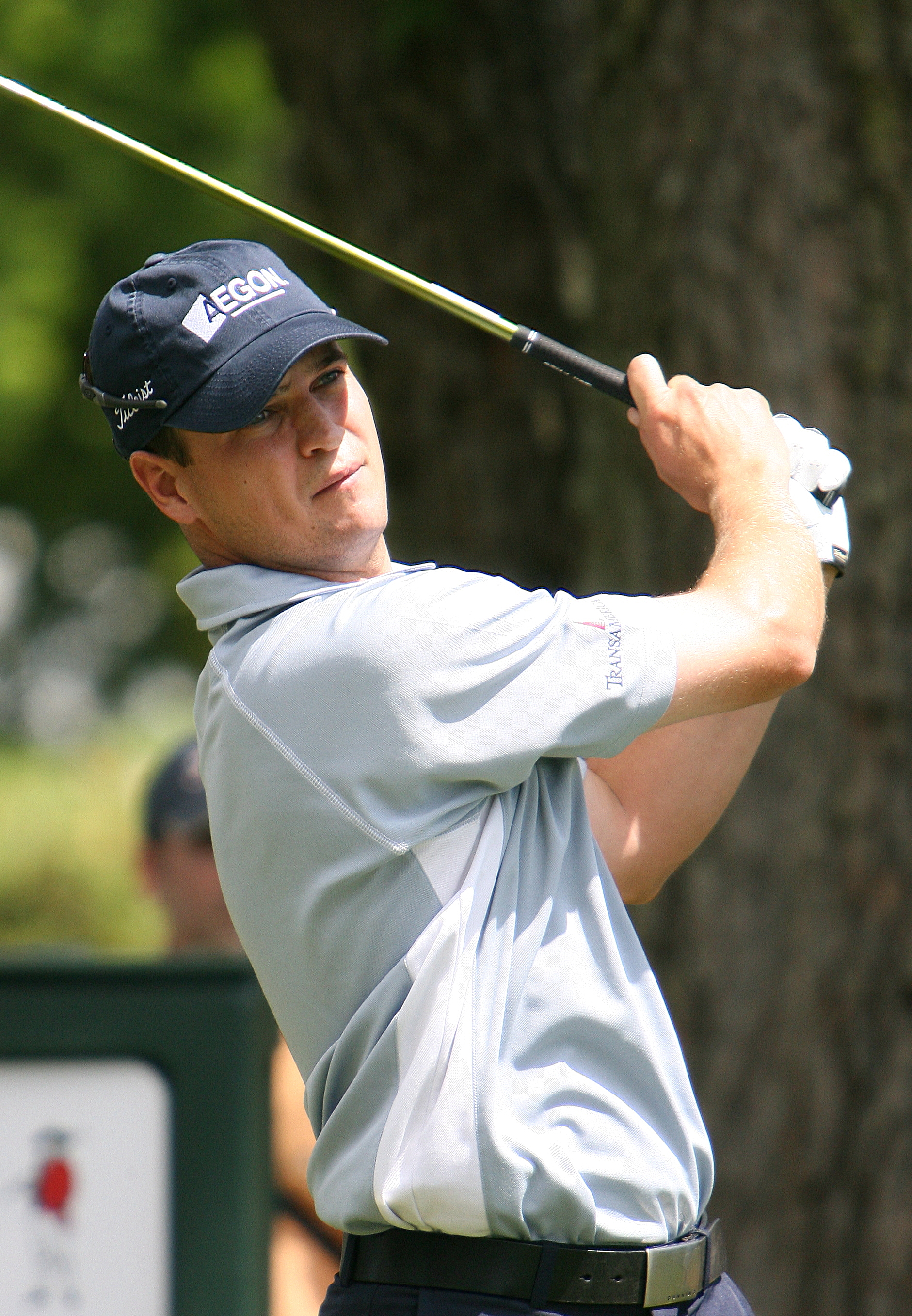 A golfer in a white polo shirt and cap mid-swing on a golf course.