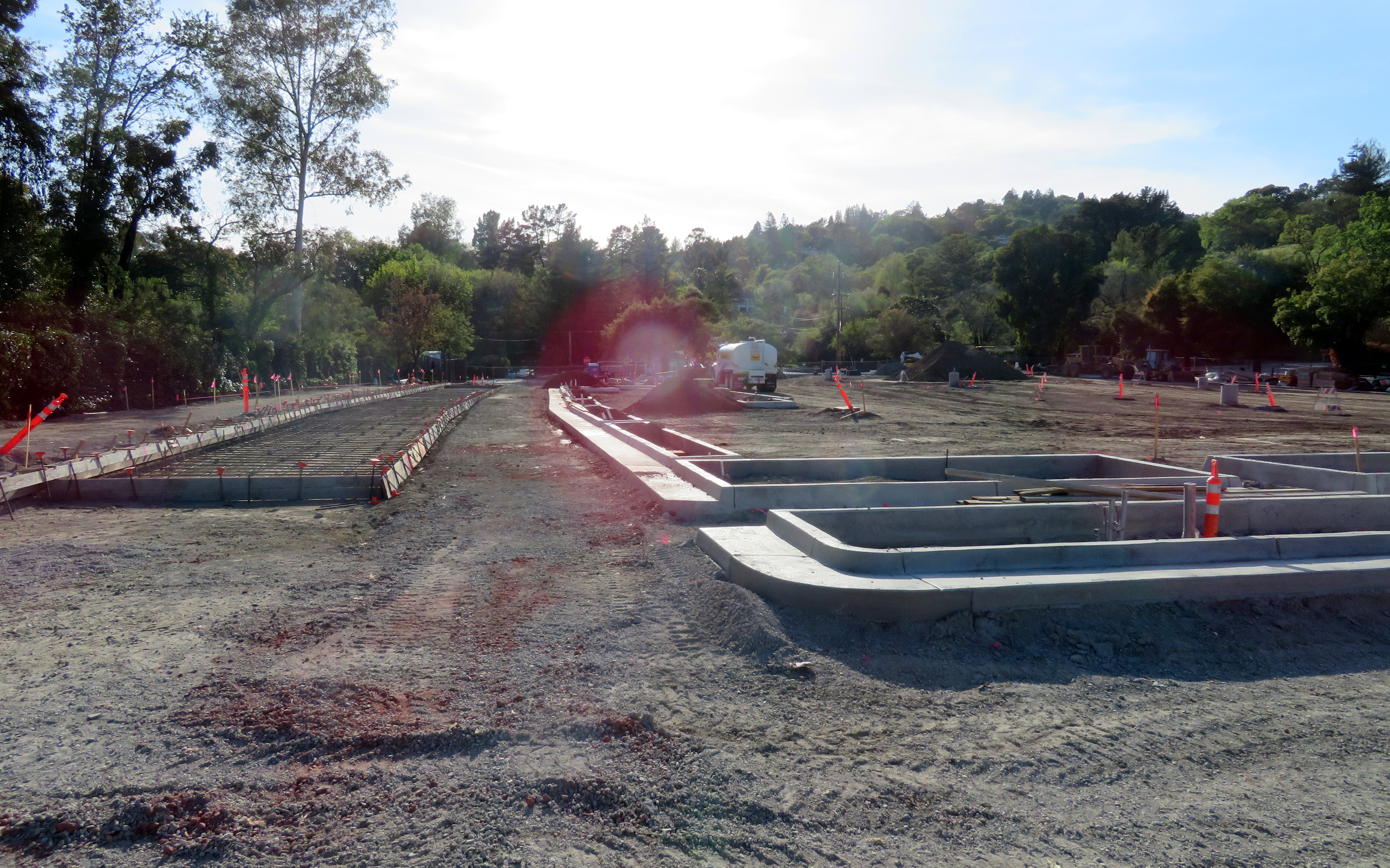 Concrete forms and graded dirt at a construction site near a transit station.