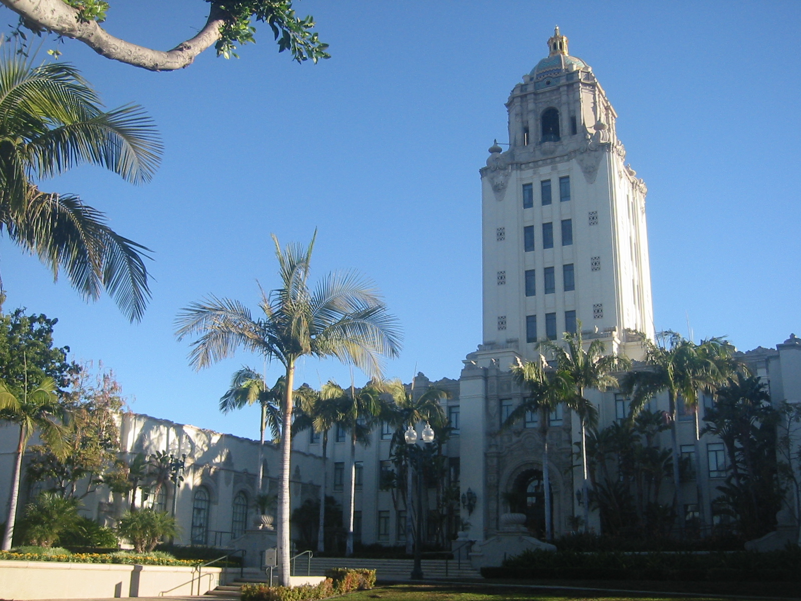 White Art Deco city hall tower surrounded by palm trees under a clear blue sky.