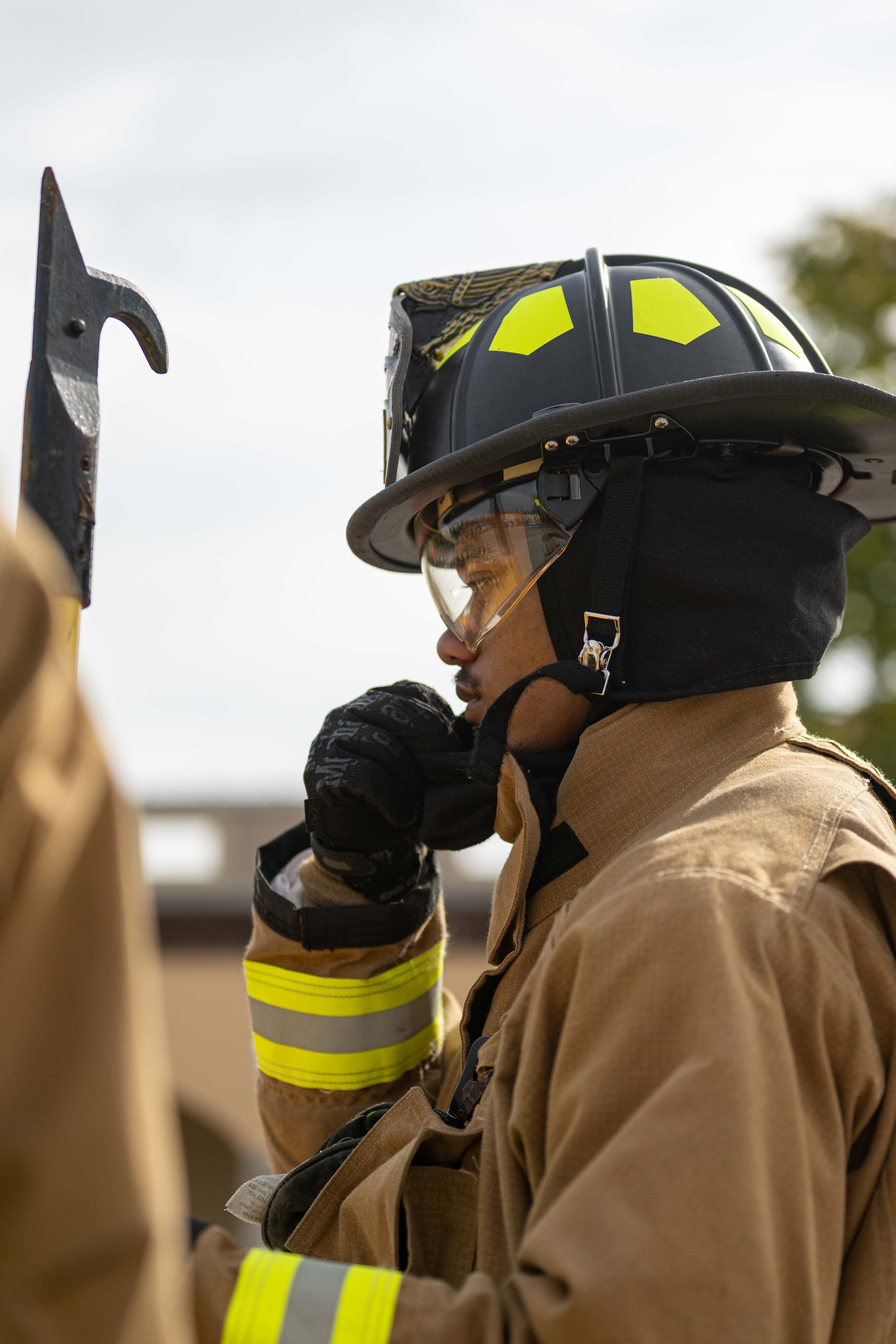 Firefighter in full turnout gear and helmet holds a tool during a fire safety demonstration.