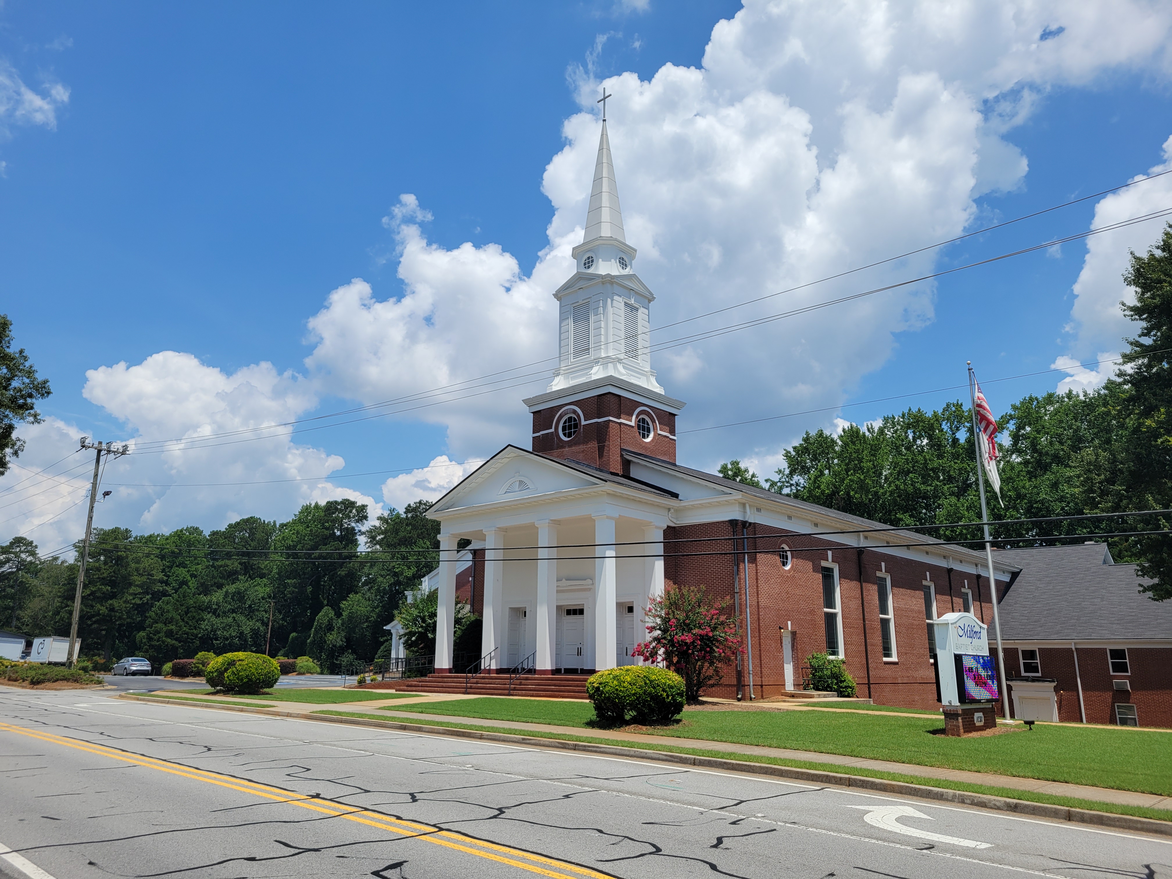 Red-brick Baptist church with white steeple and columned entrance portico, American flag on a flagpole.