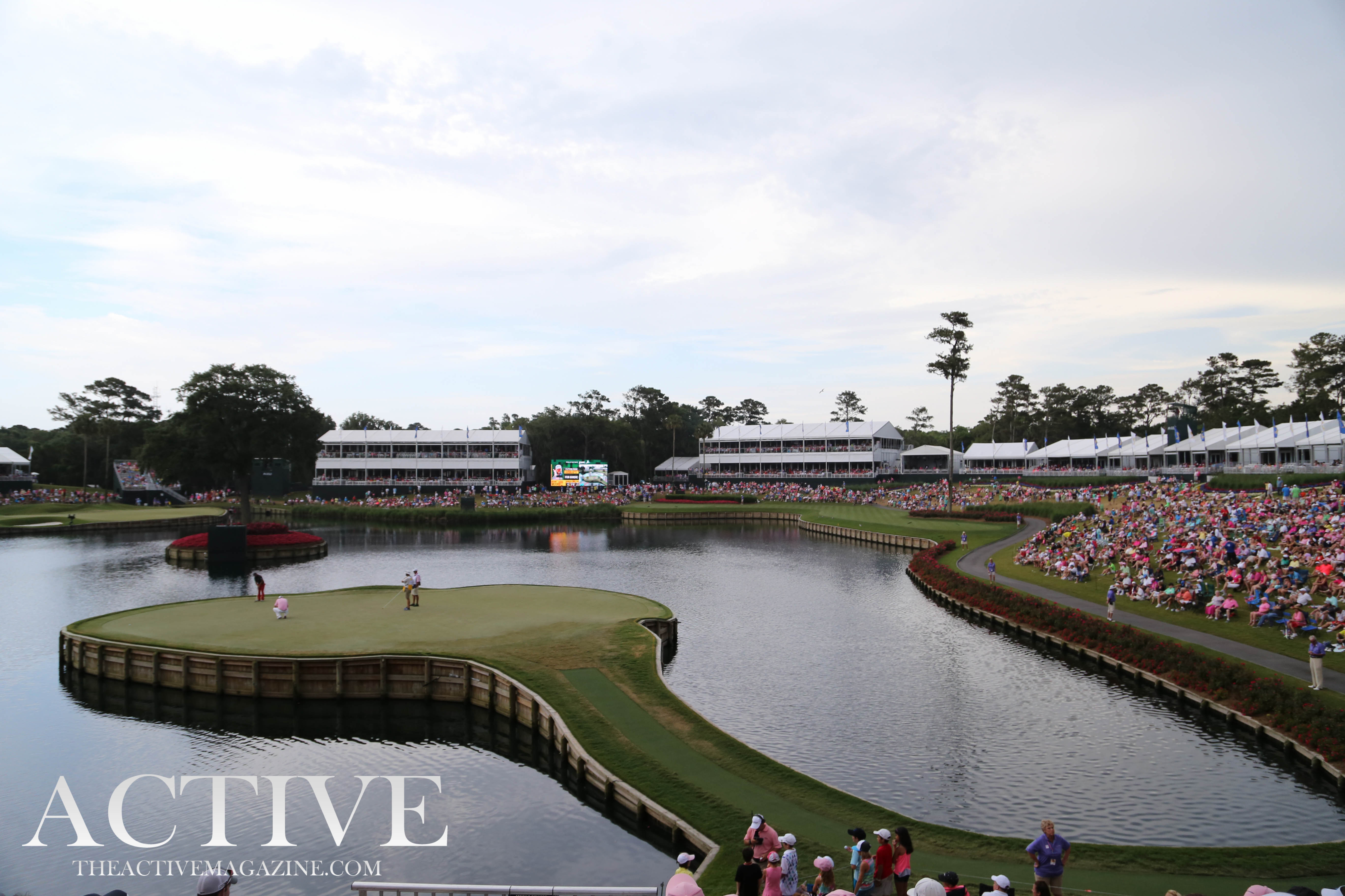 Aerial view of an island green surrounded by water with packed grandstands and spectators.