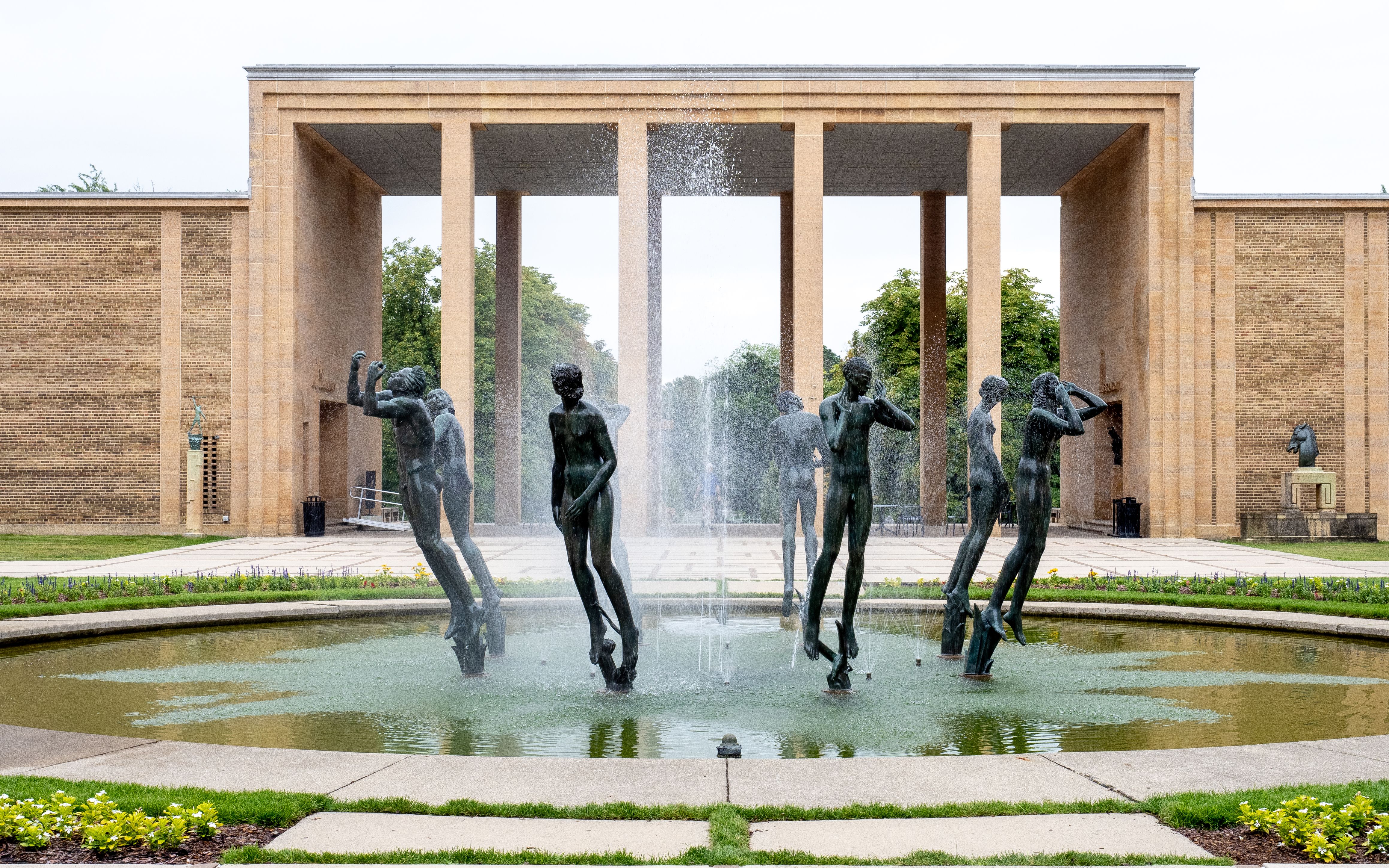 Stone museum building with colonnaded facade, reflecting pool, fountain, and bronze sculptures.