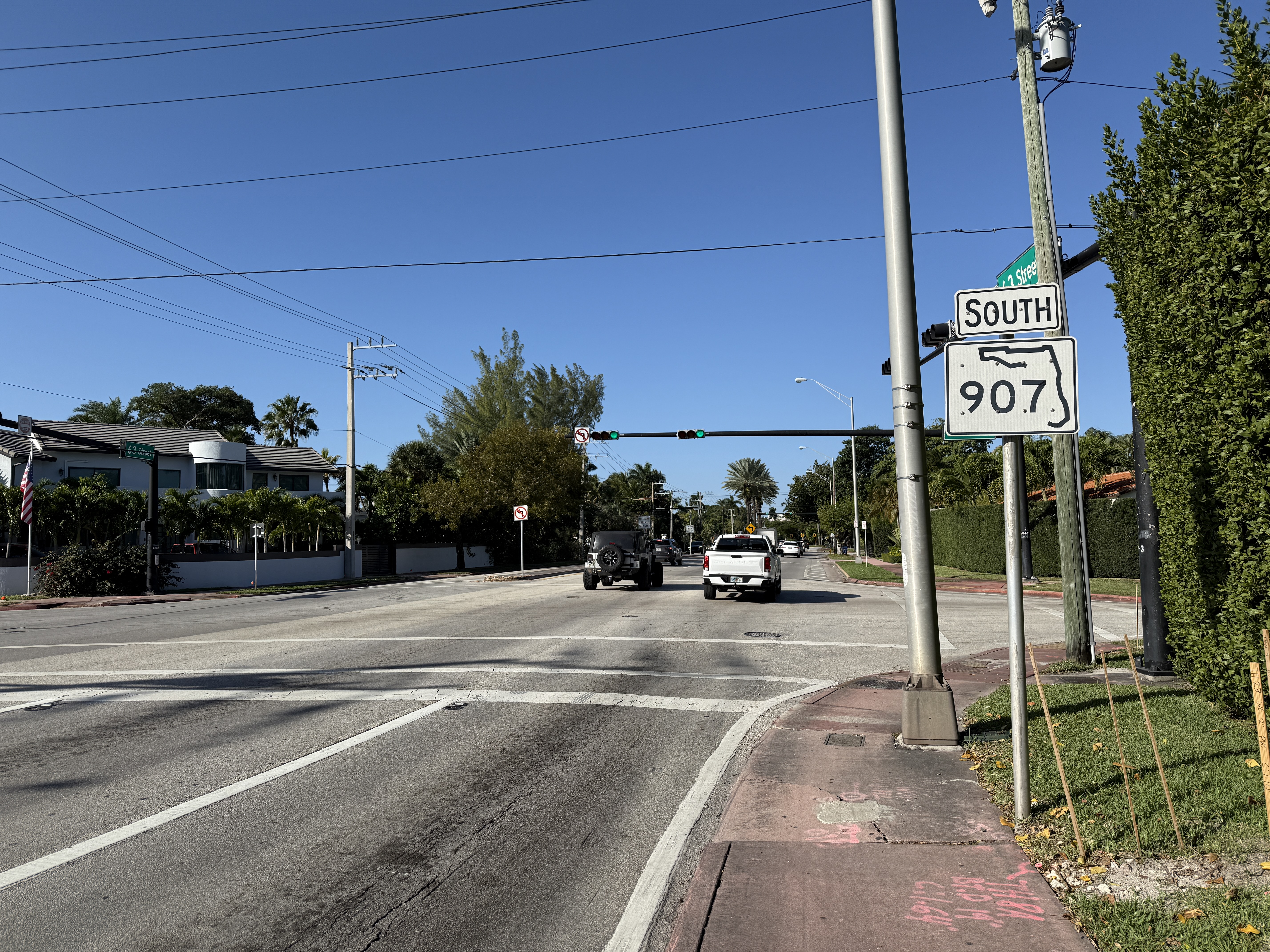 A traffic signal on a mast arm over a multi-lane Miami Beach intersection with palm trees.