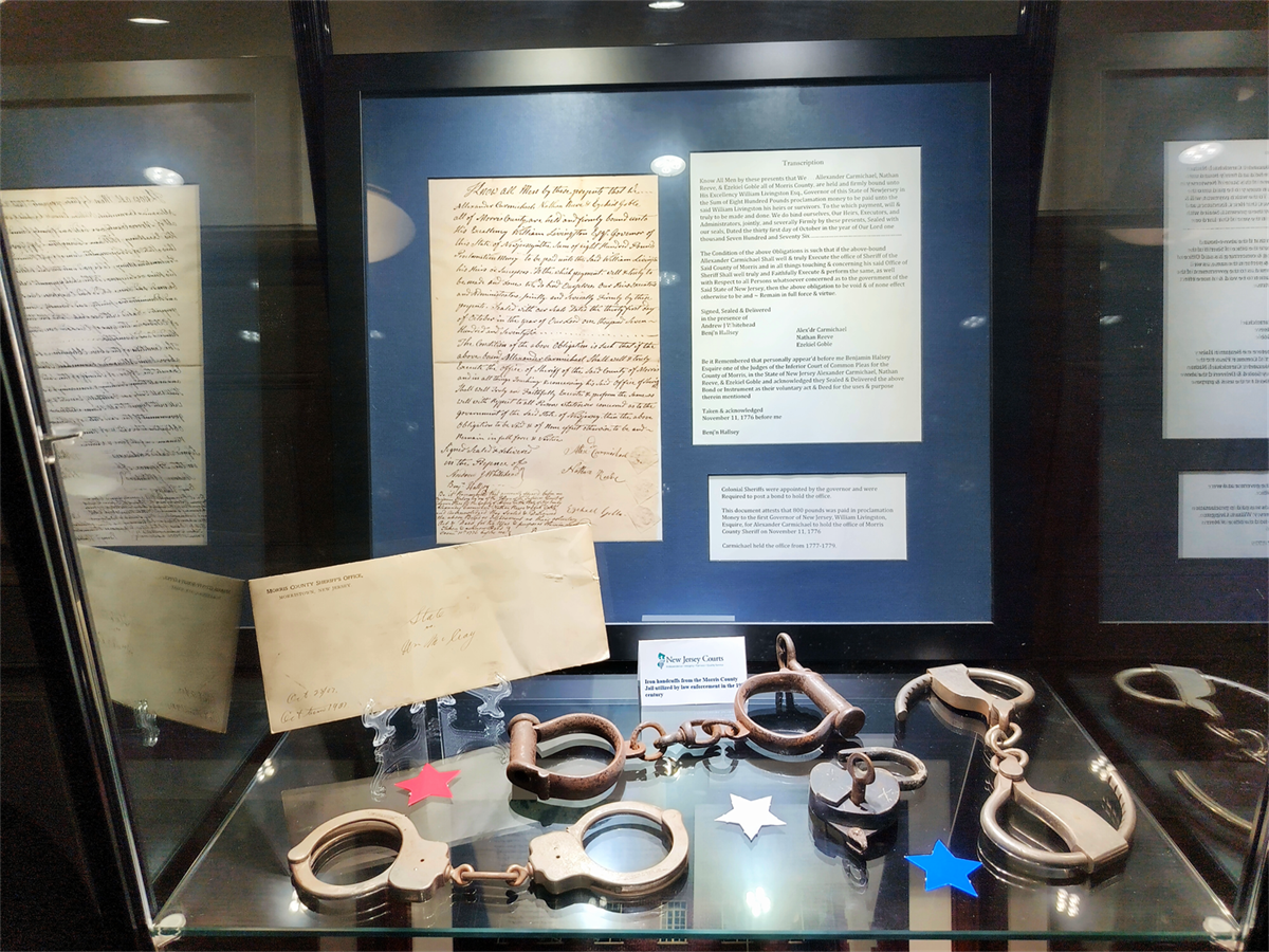 Glass display case containing historical handcuffs, shackles, and handwritten documents.