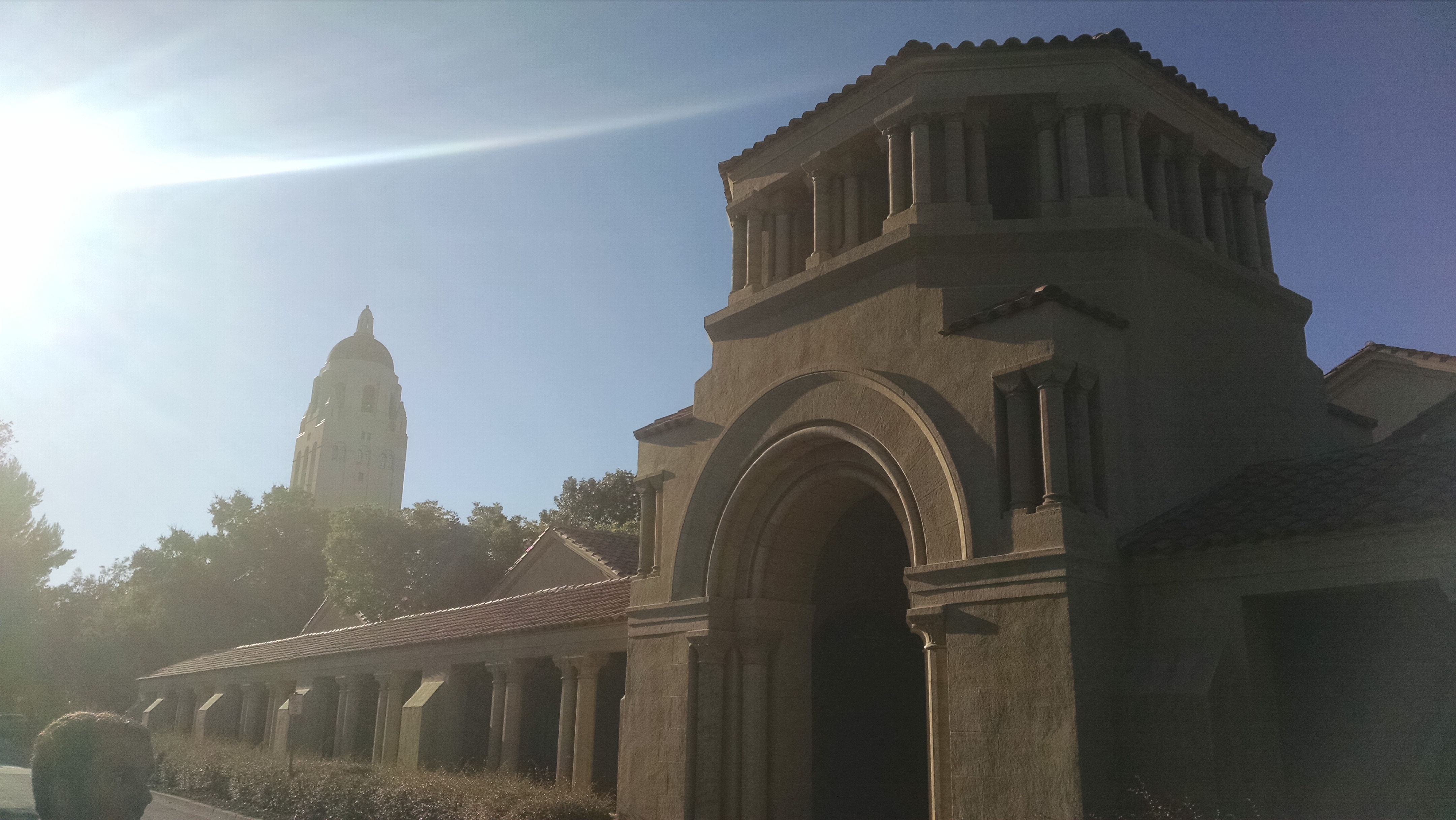 Sandstone building with large arched entryway on a university campus in bright sunlight.