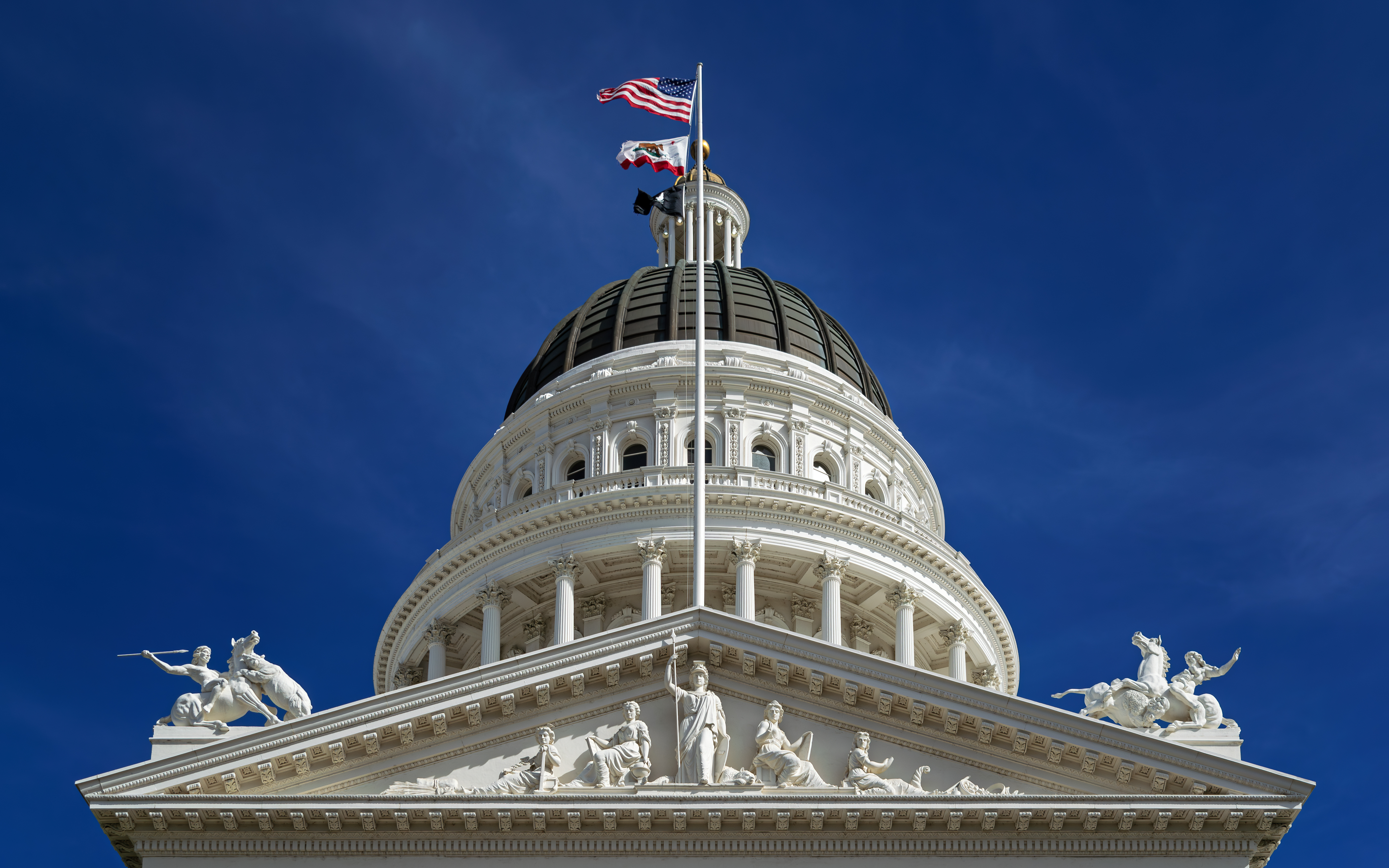 Upward view of the California State Capitol dome and rotunda against a deep blue sky.
