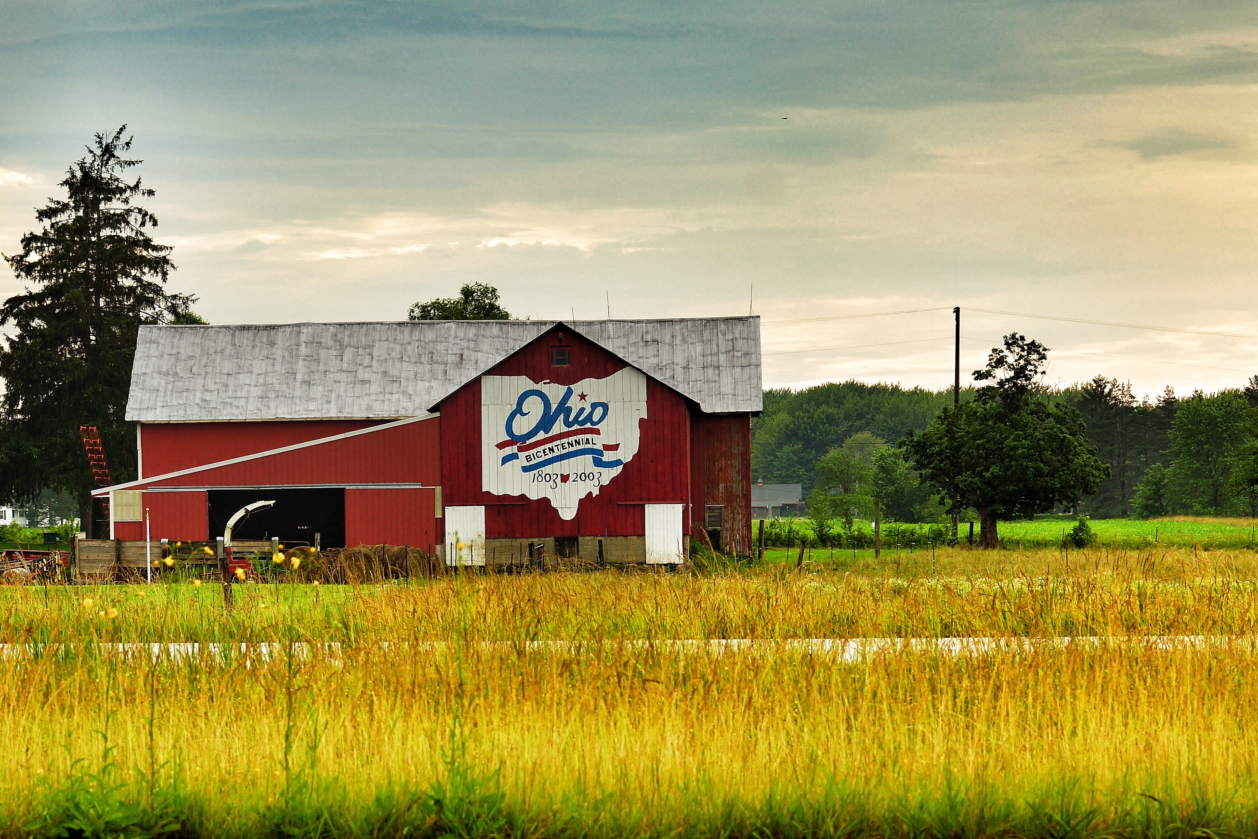 Red barn with Ohio Bicentennial logo painted on its side under a partly cloudy sky.