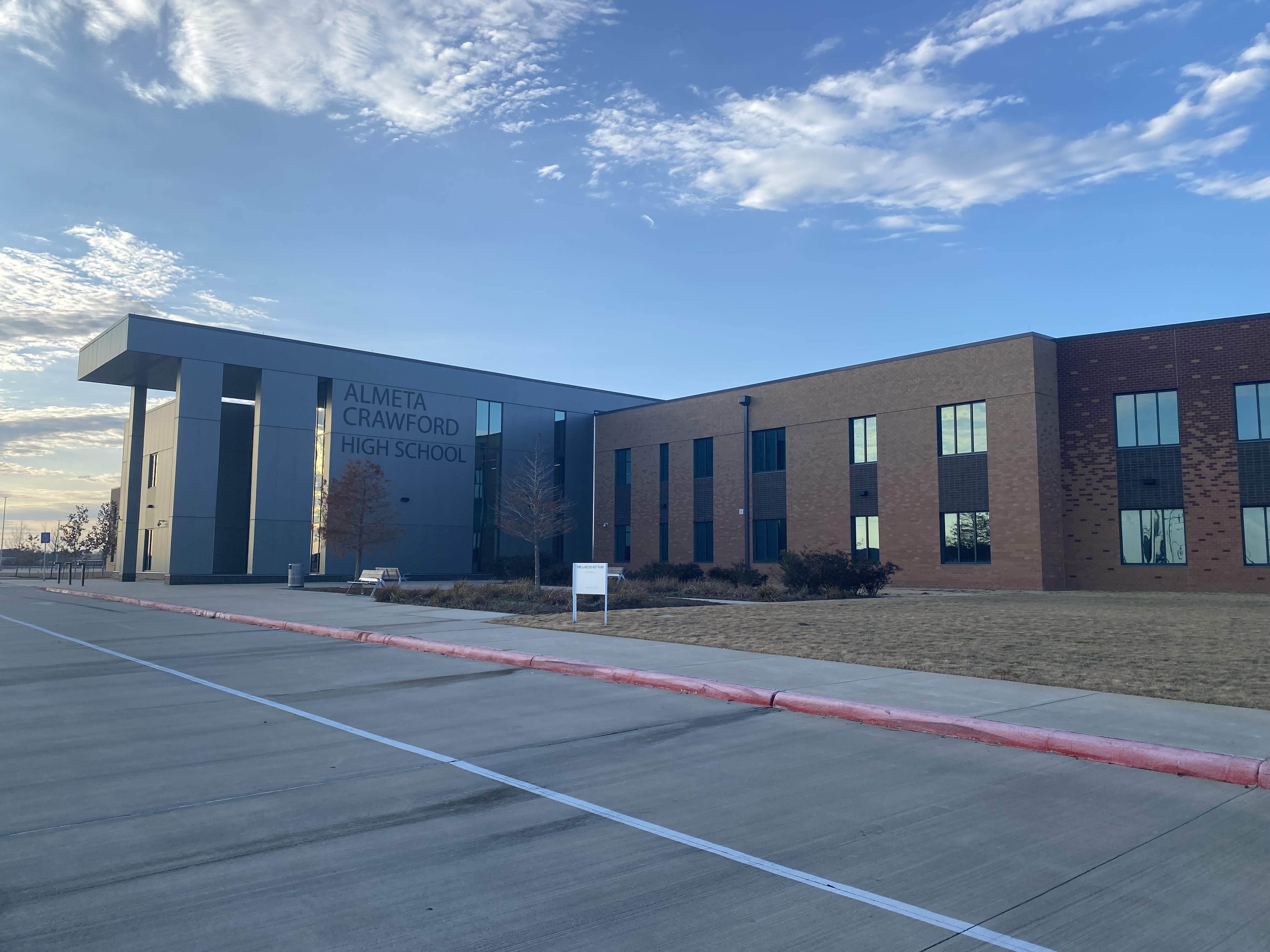 Modern brick and metal-panel high school building with signage under partly cloudy sky.