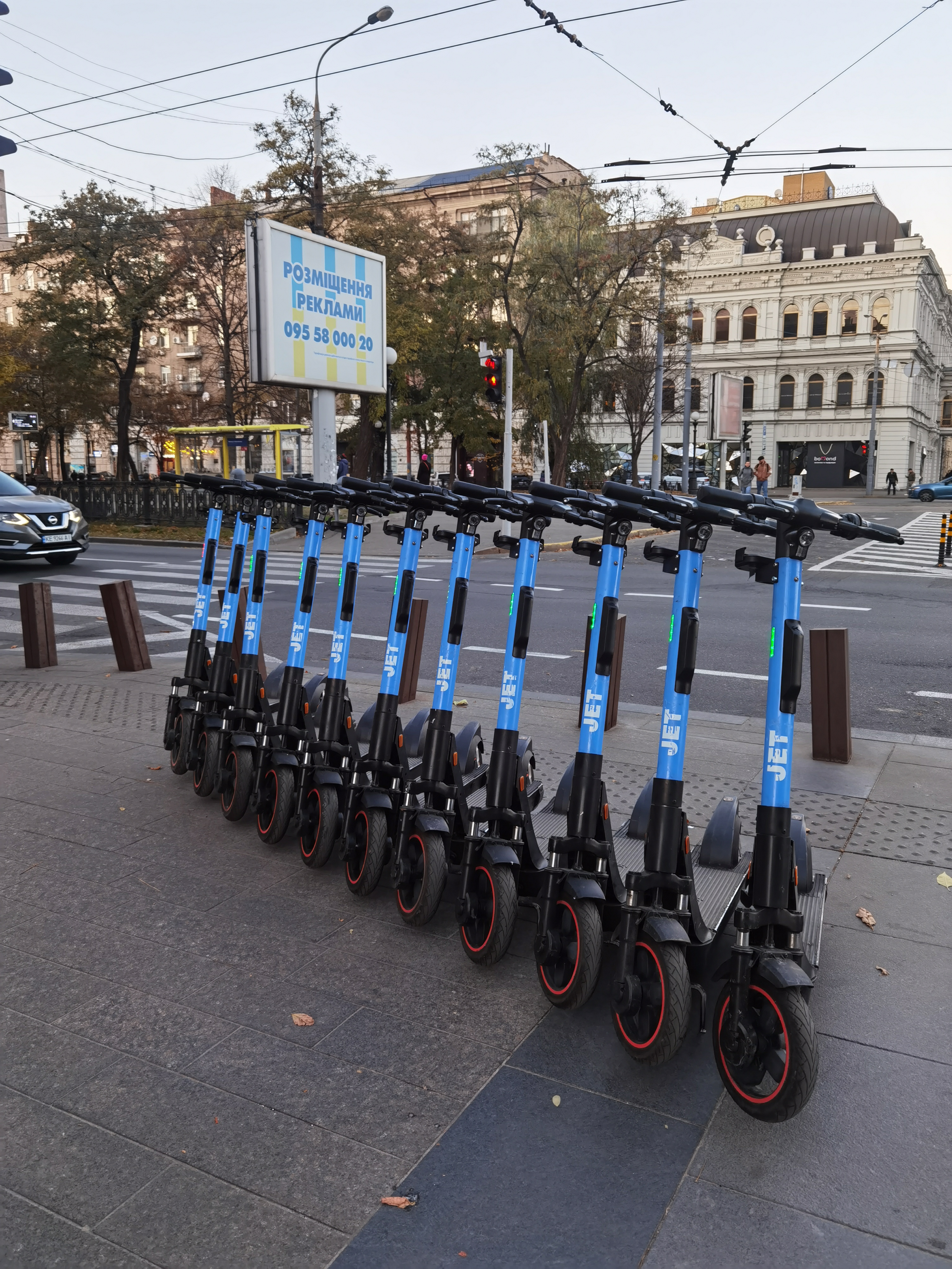 A row of blue-and-black electric kick scooters parked along a sidewalk.
