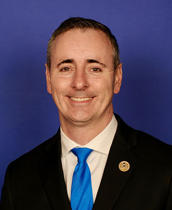 Formal congressional portrait of a man in a dark suit and blue tie against a blue background.