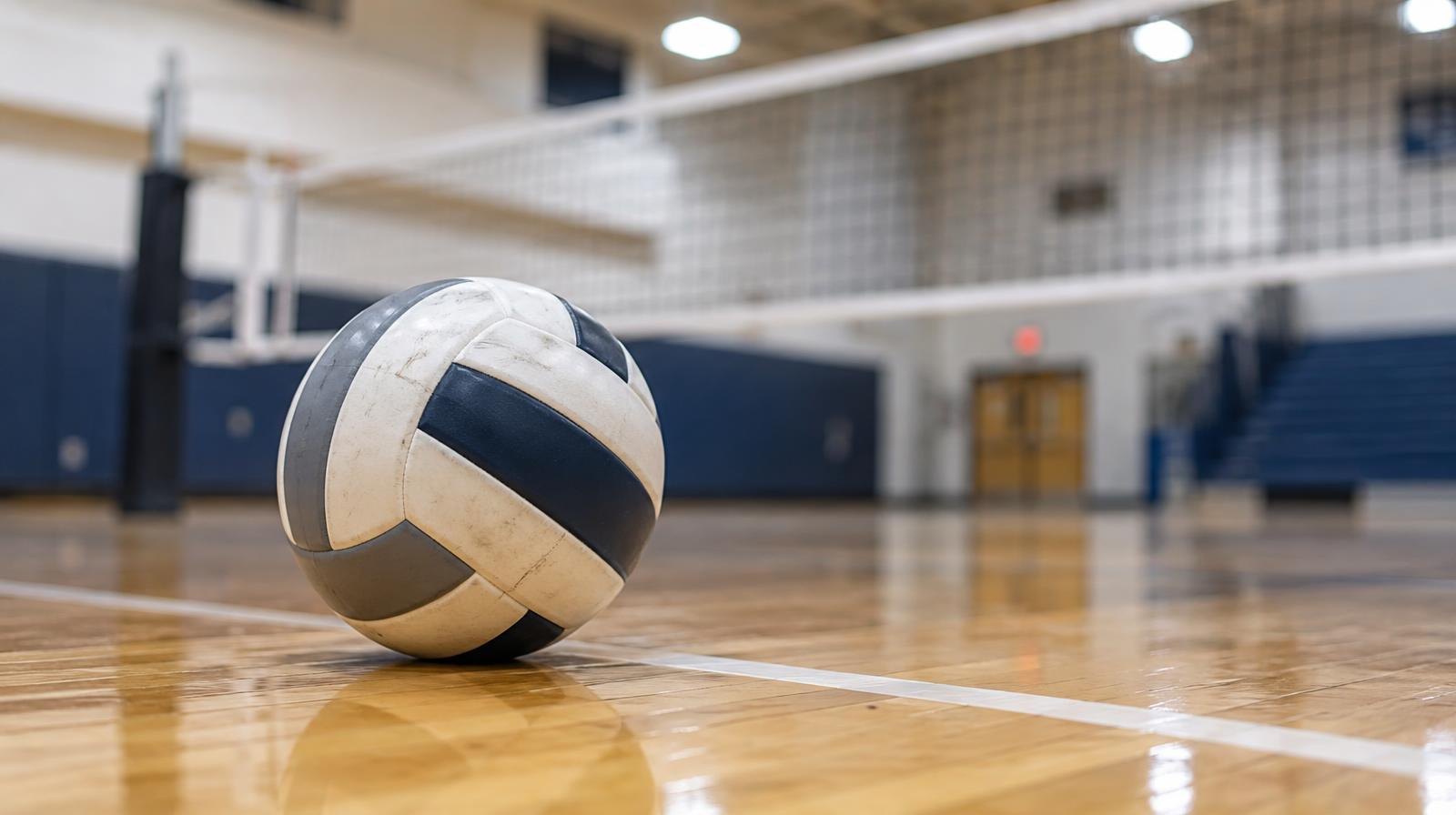 A volleyball sitting on a hardwood gym floor near the net.