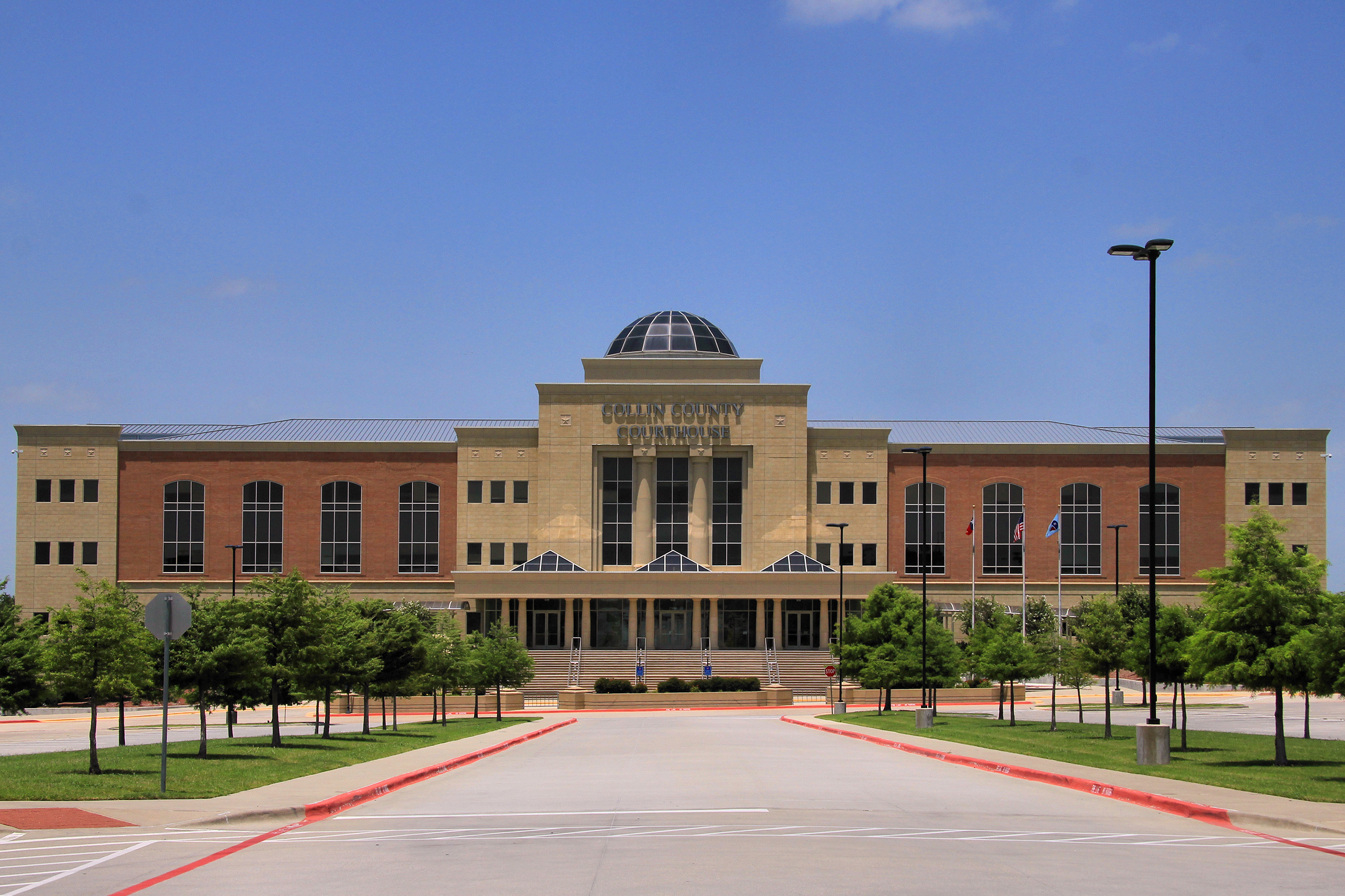 Brick courthouse with a central dome and paved plaza under a clear blue sky.