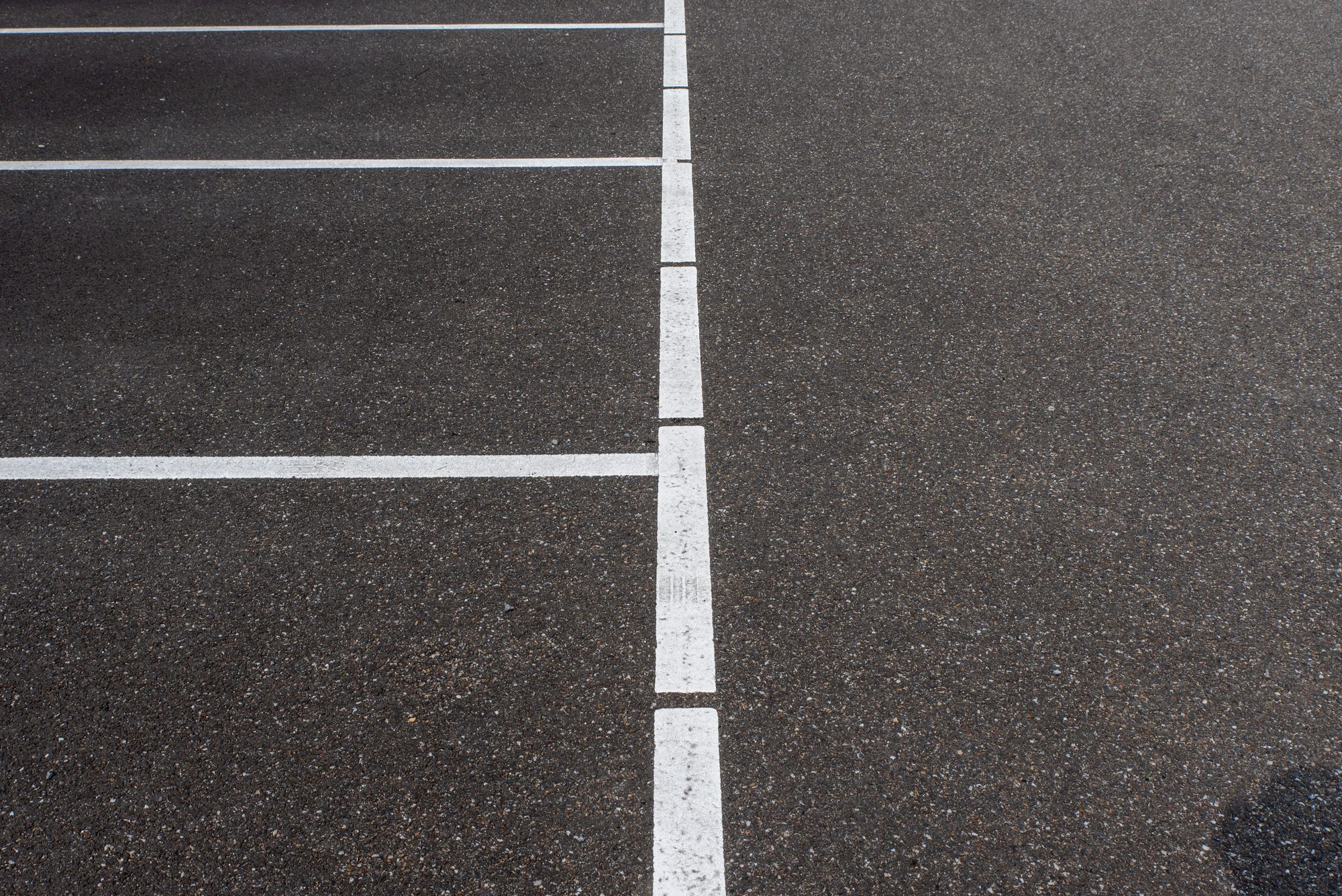 Asphalt parking lot showing white lines marking parking spaces. Minimalist urban scene.