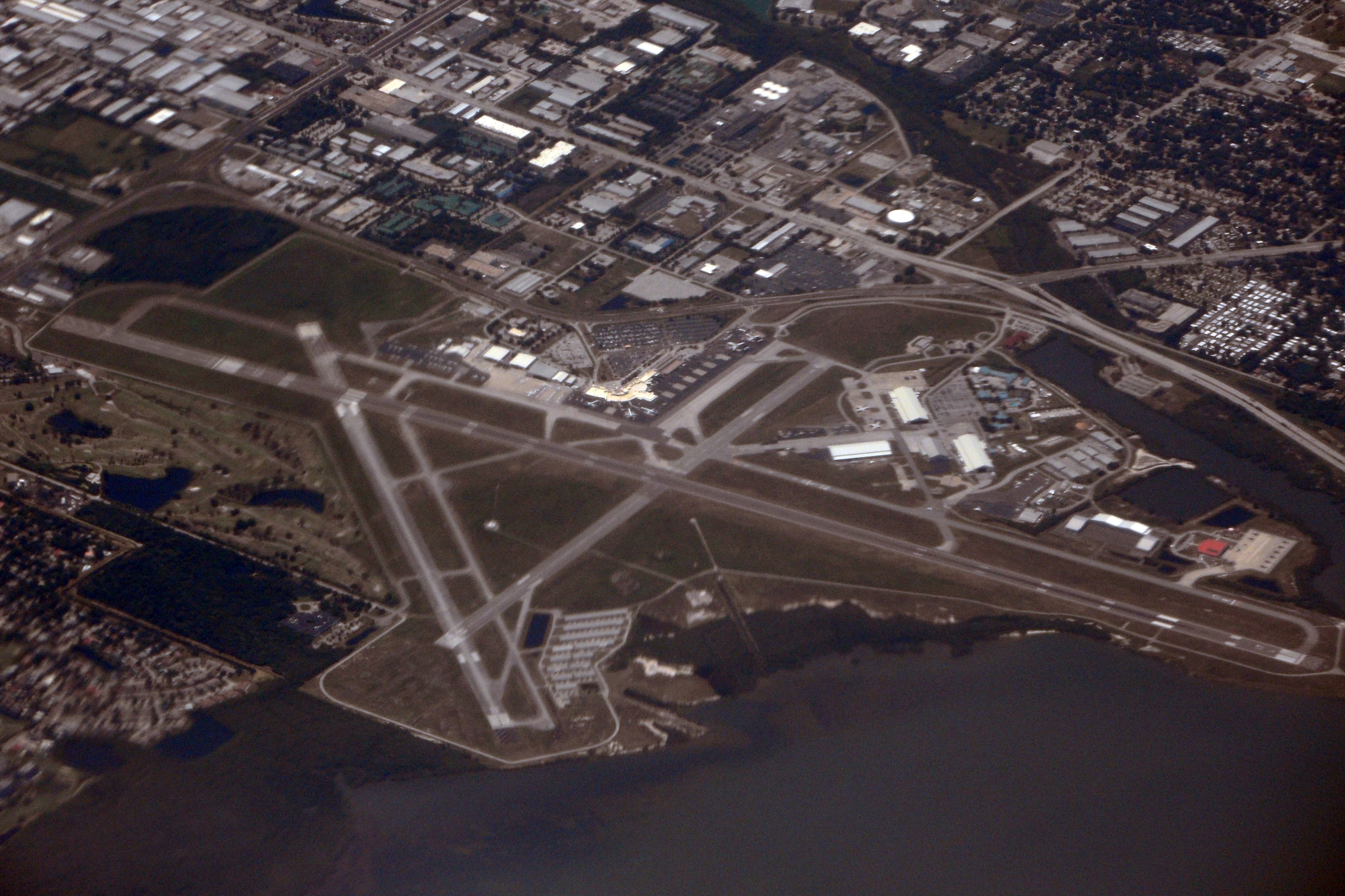 Aerial view of an airport with intersecting runways, terminal buildings, and surrounding water.