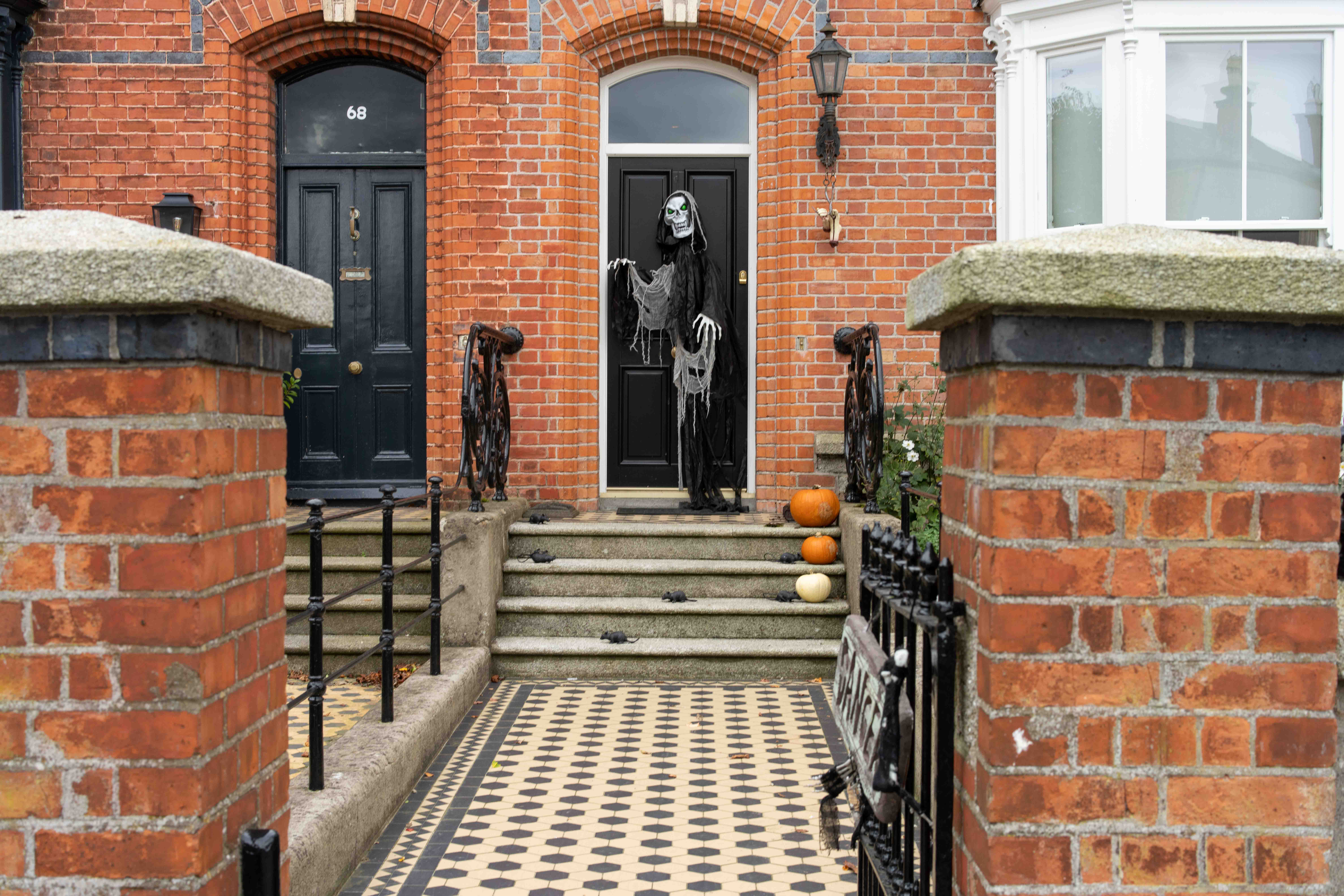 Brick house entrance with a skeleton on the door and pumpkins on the steps.