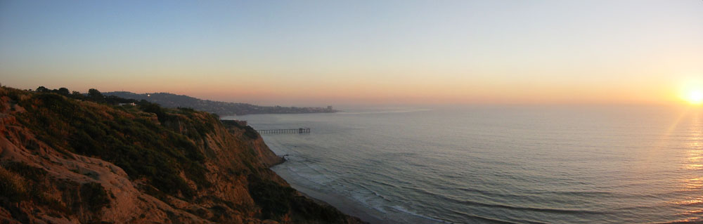Panoramic coastal view at sunset with a long pier extending into the ocean.