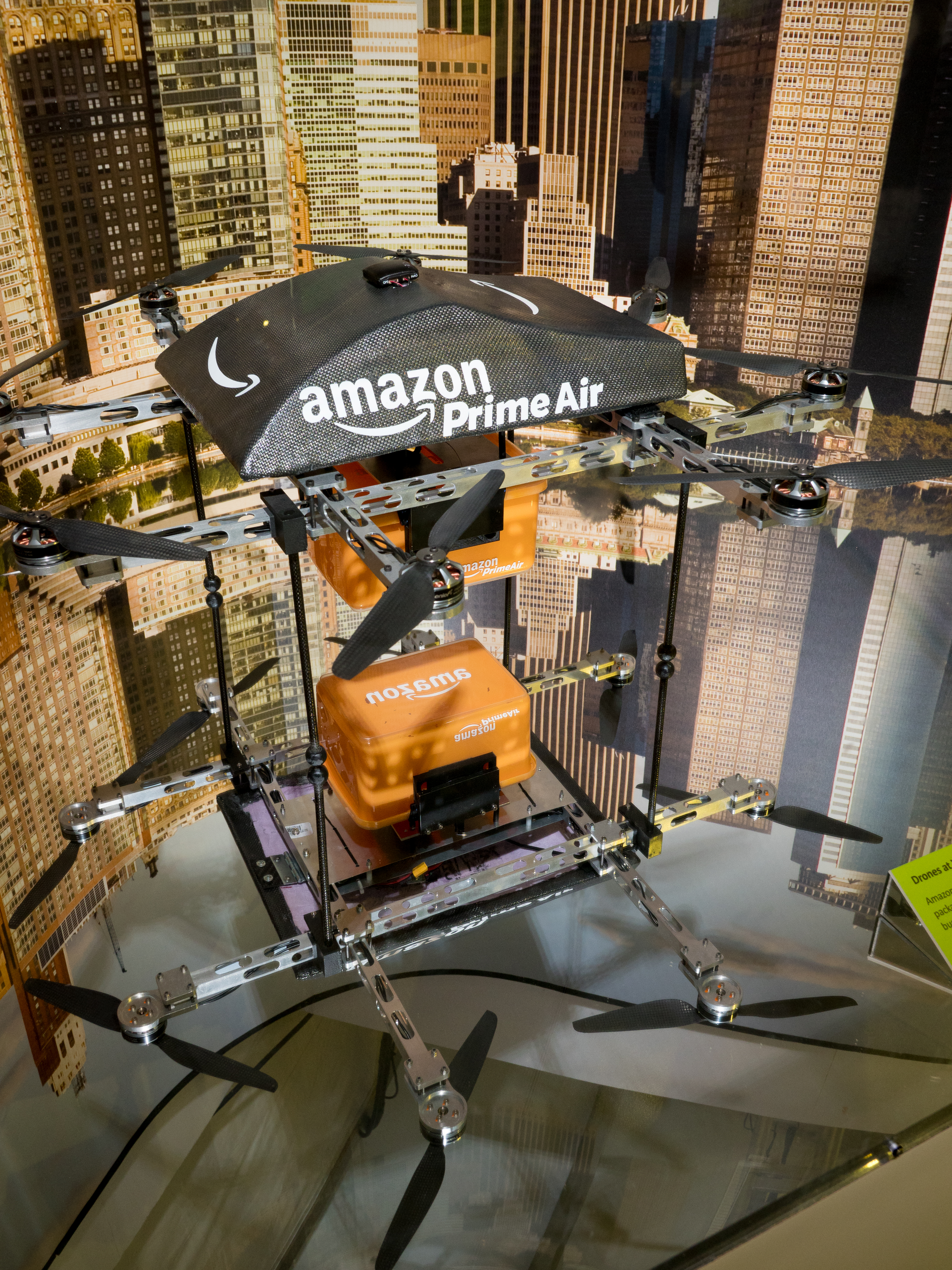 Amazon Prime Air octocopter drone with an orange package hanging beneath it on display.