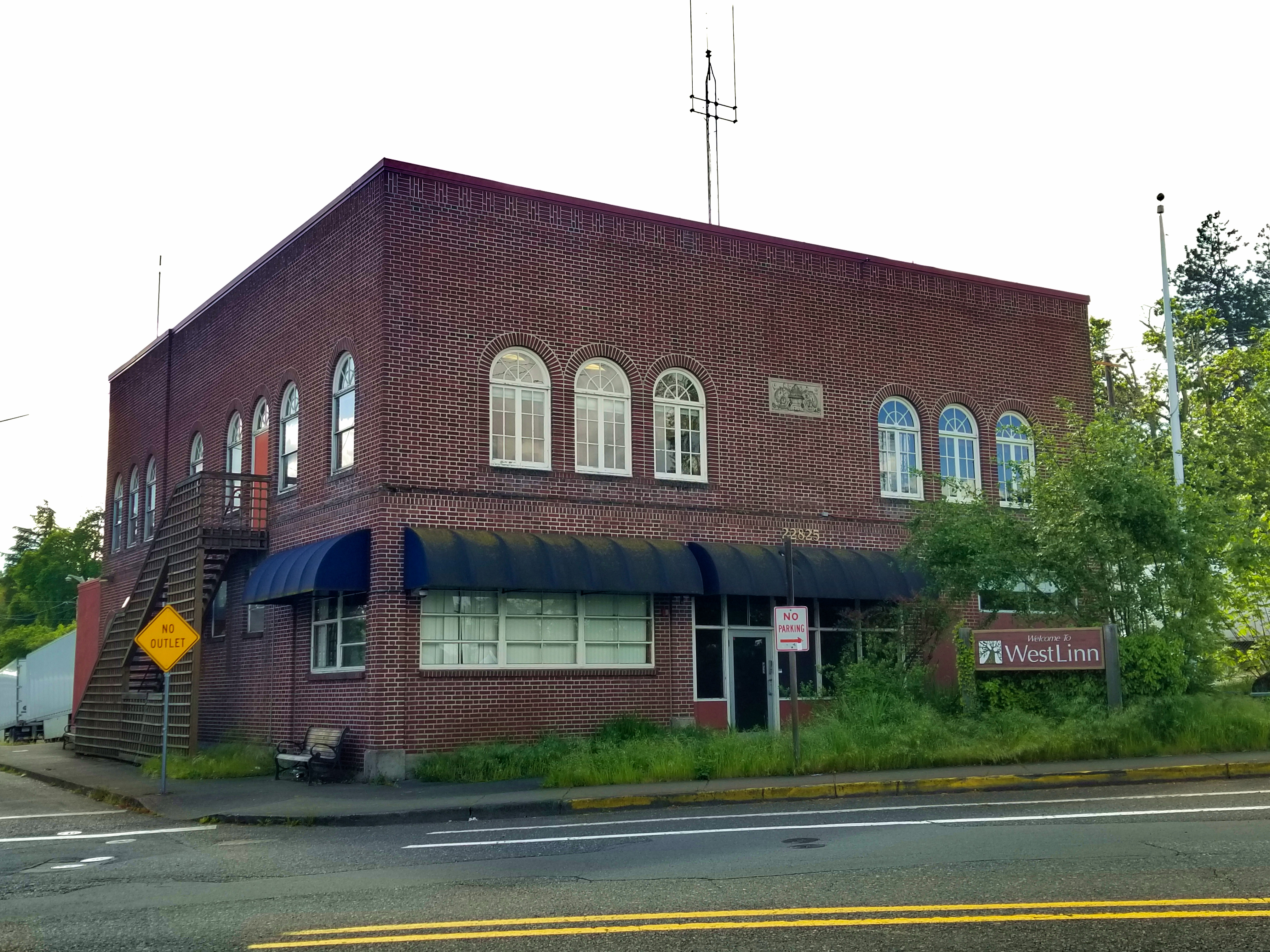 Two-story red brick building with arched windows and blue awnings on a street corner.