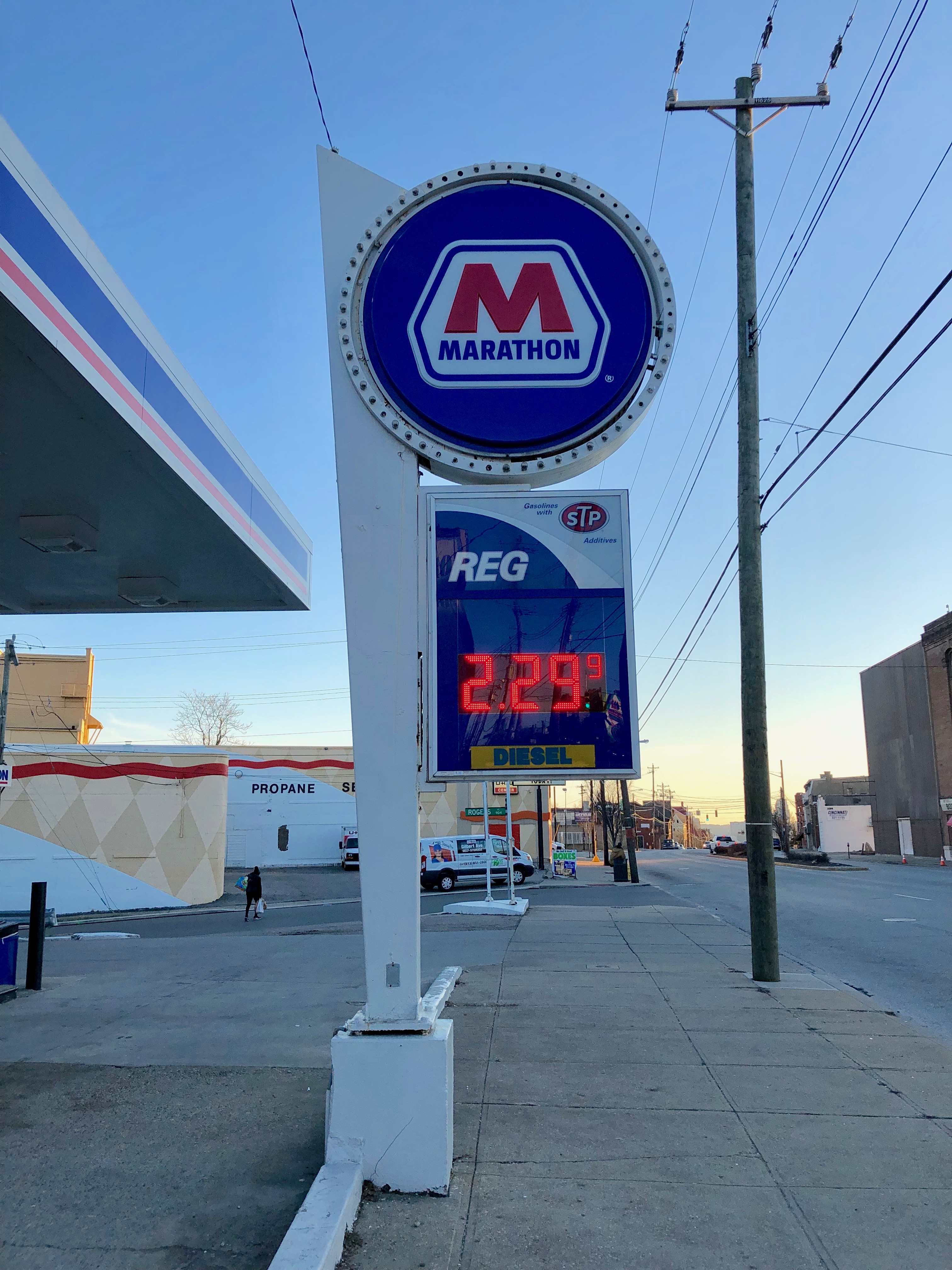 A Marathon gas station price sign on a city street, canopy visible behind it.