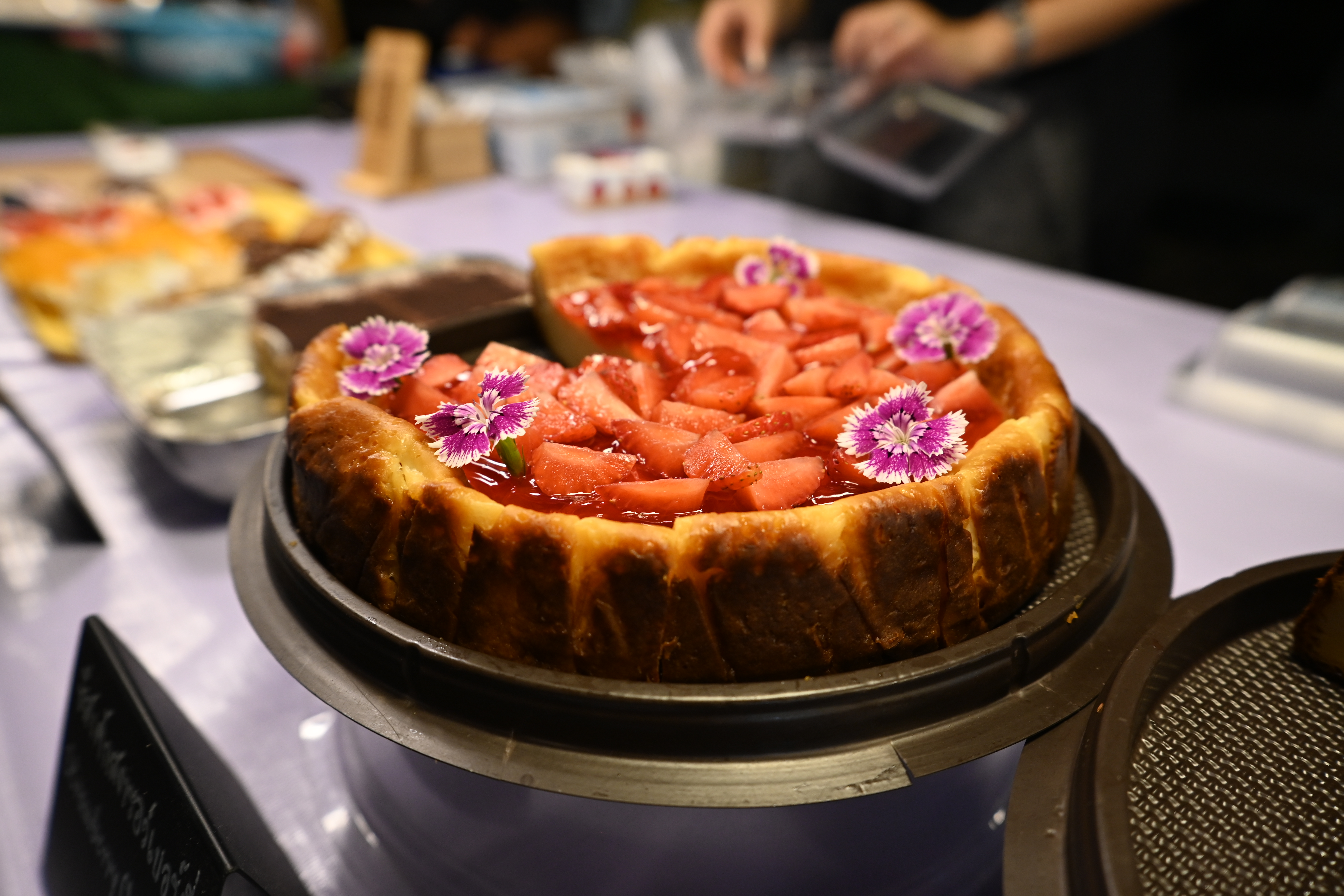 A decorated strawberry cheesecake on a stand at a bakery display counter.