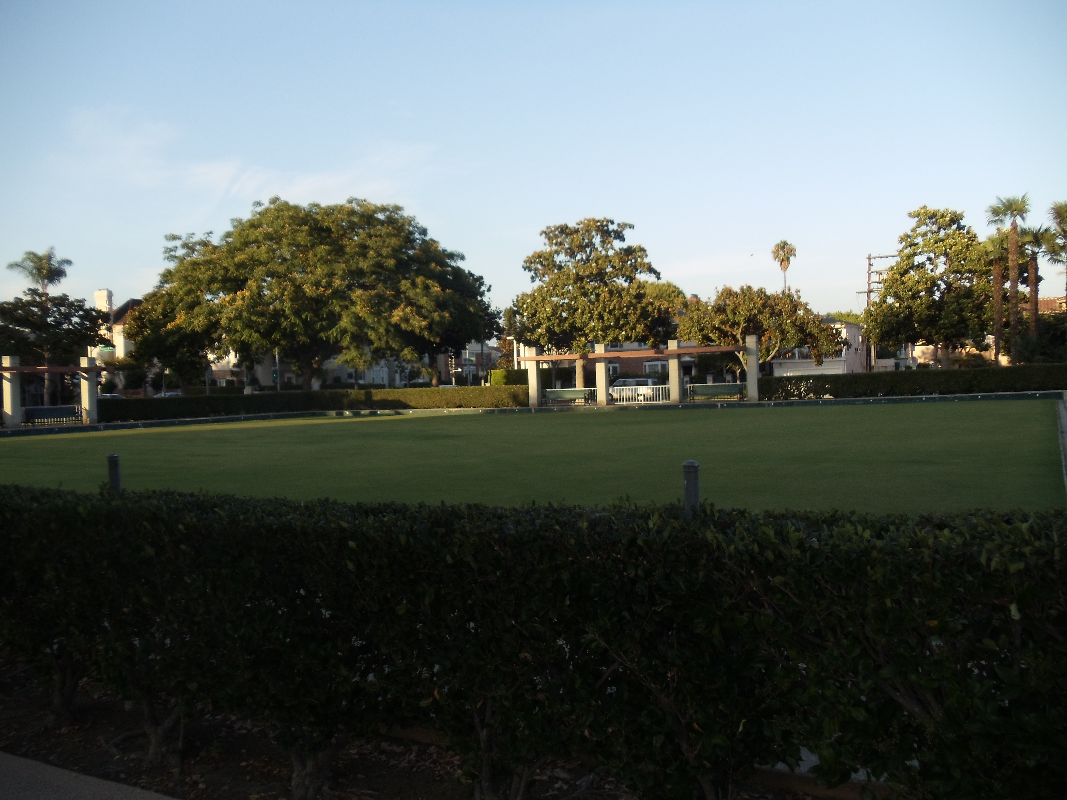 Manicured lawn bowling green bordered by hedges and shade trees in a Beverly Hills park.