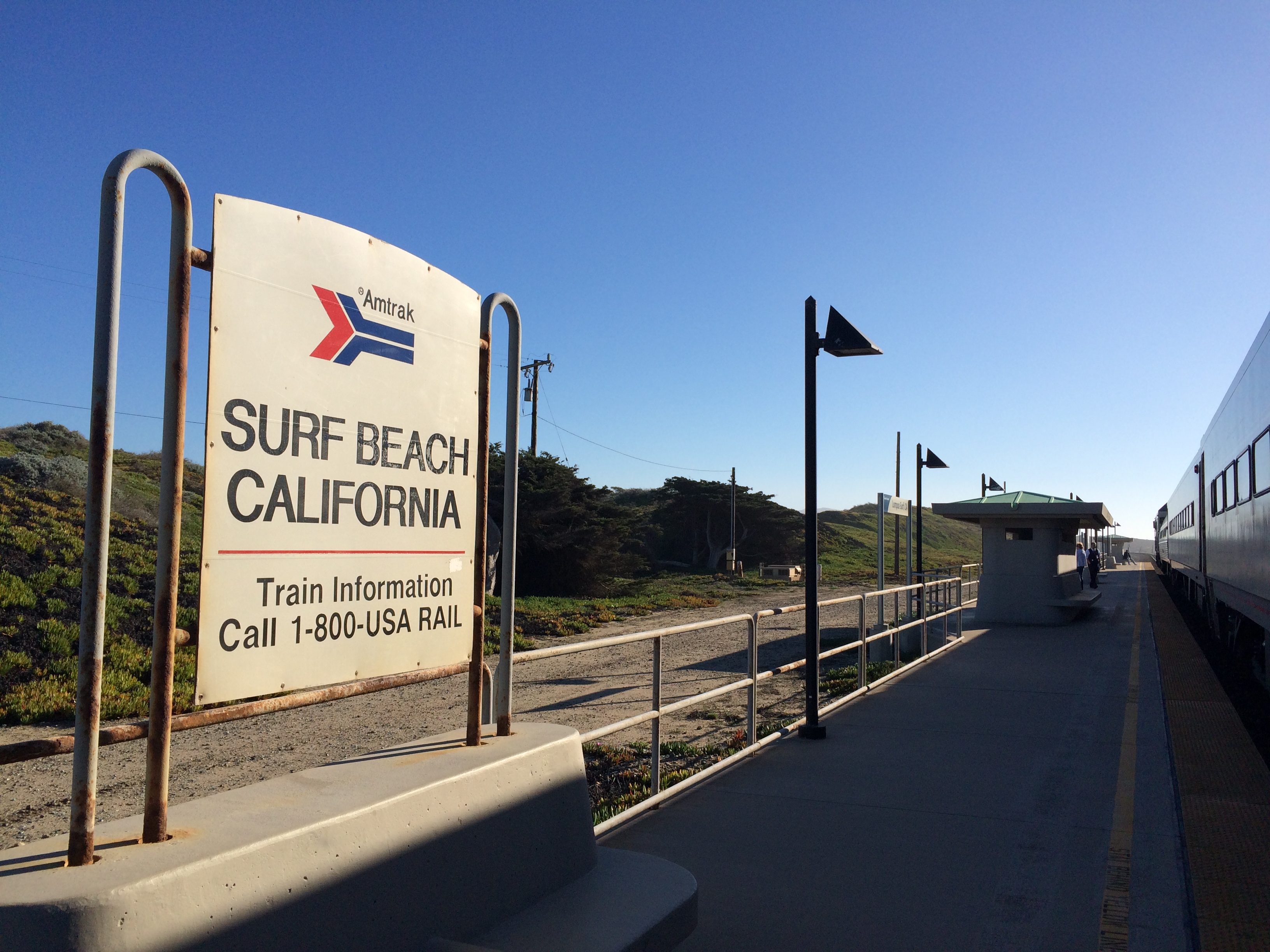 Amtrak station sign and train on track under a clear blue sky.