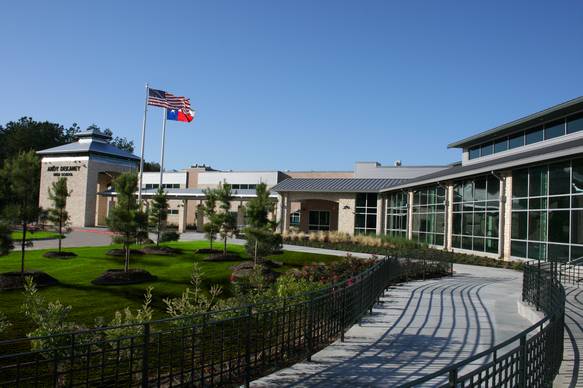 Front exterior of a modern high school building with flagpoles and a curved walkway.