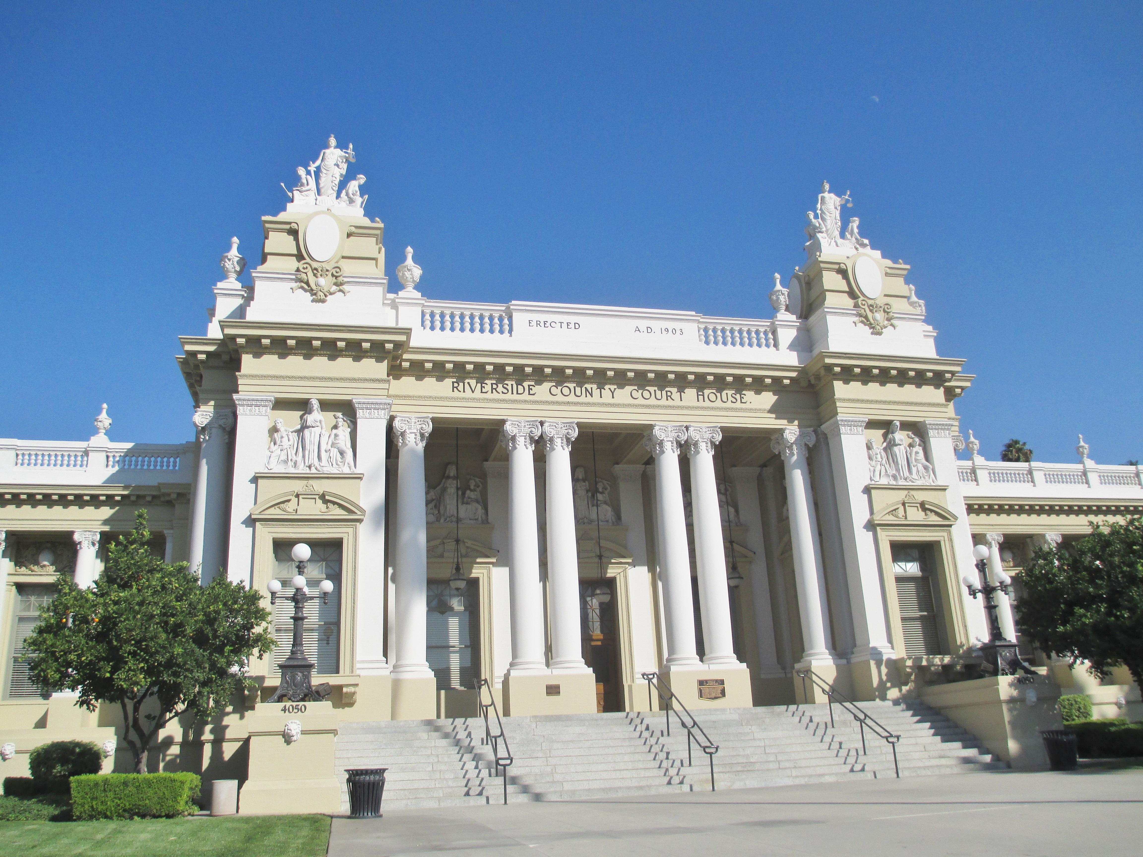 Neoclassical courthouse building with white columns and ornate statuary under a blue sky.