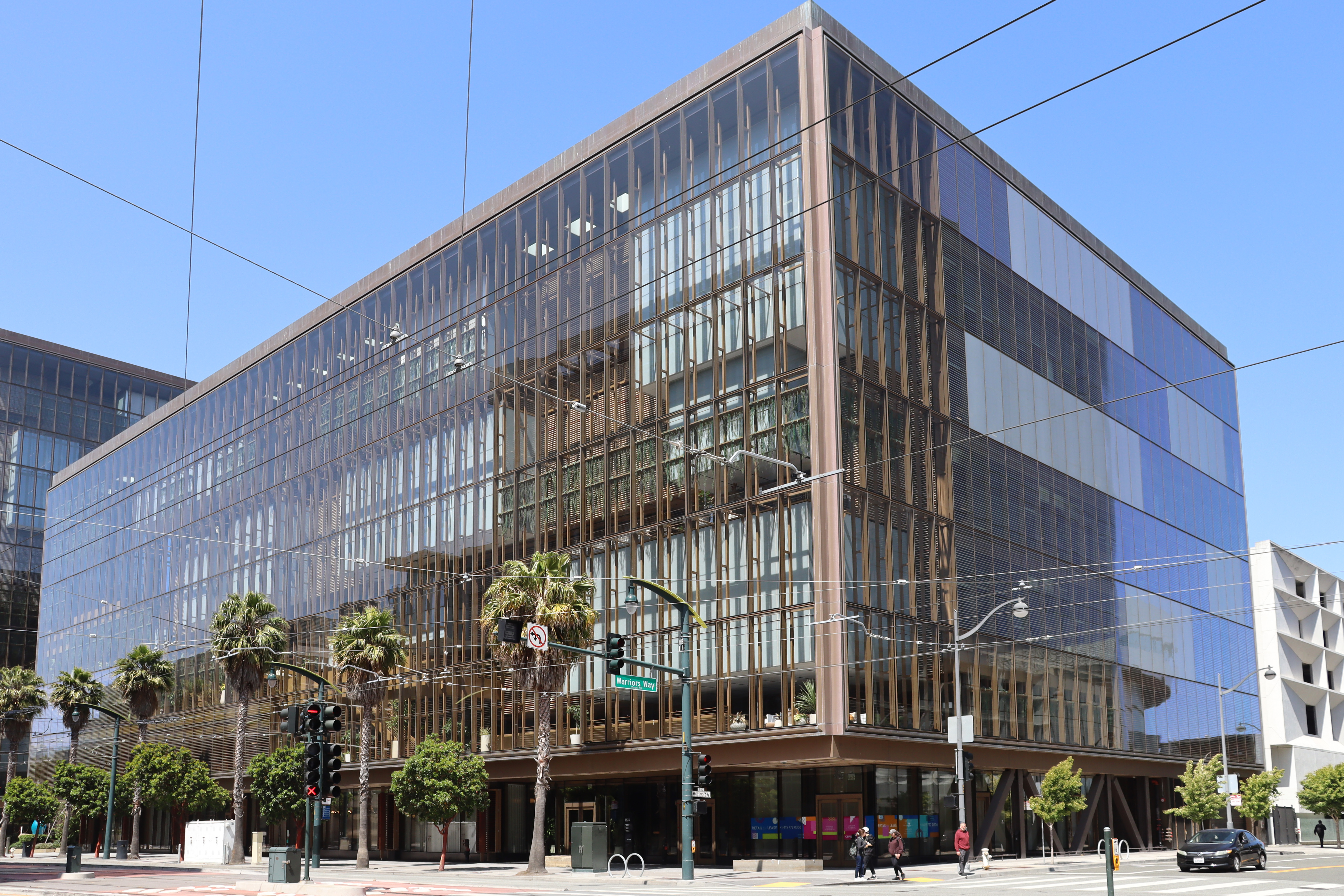 Modern glass and bronze office building on a street corner lined with palm trees.