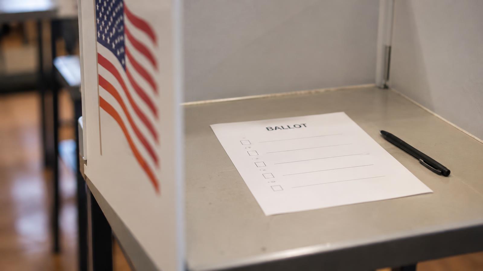 A blank paper ballot resting in a voting booth with a pen beside it.
