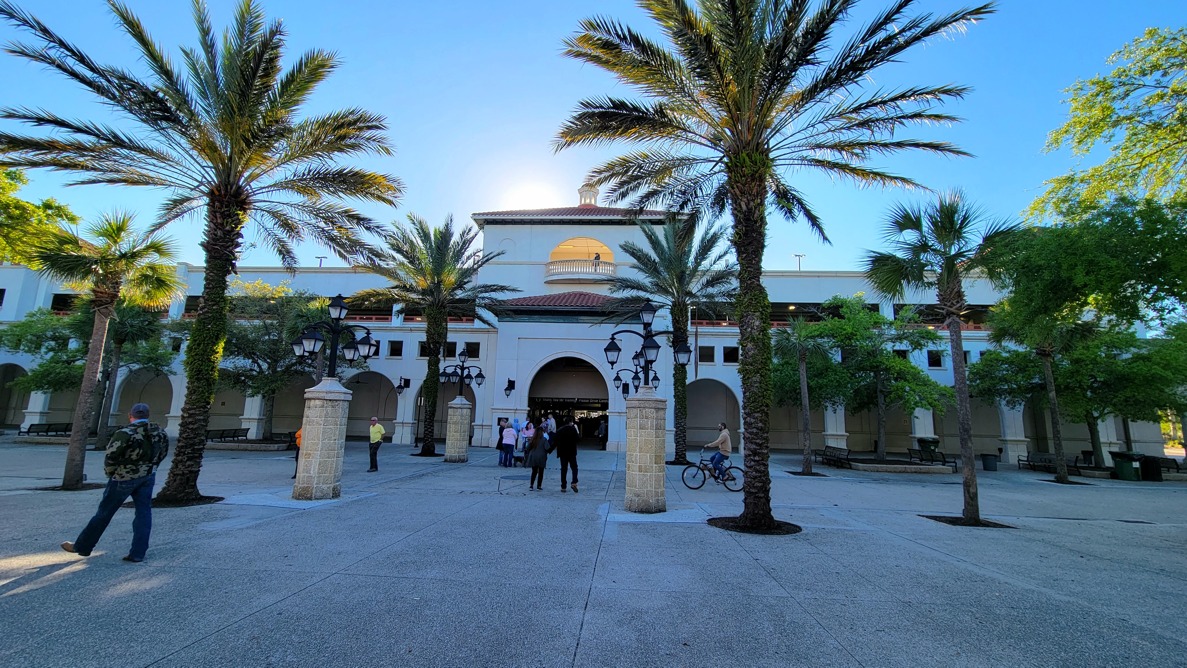 White stucco building with arched colonnades and palm trees lining a wide plaza at dusk.