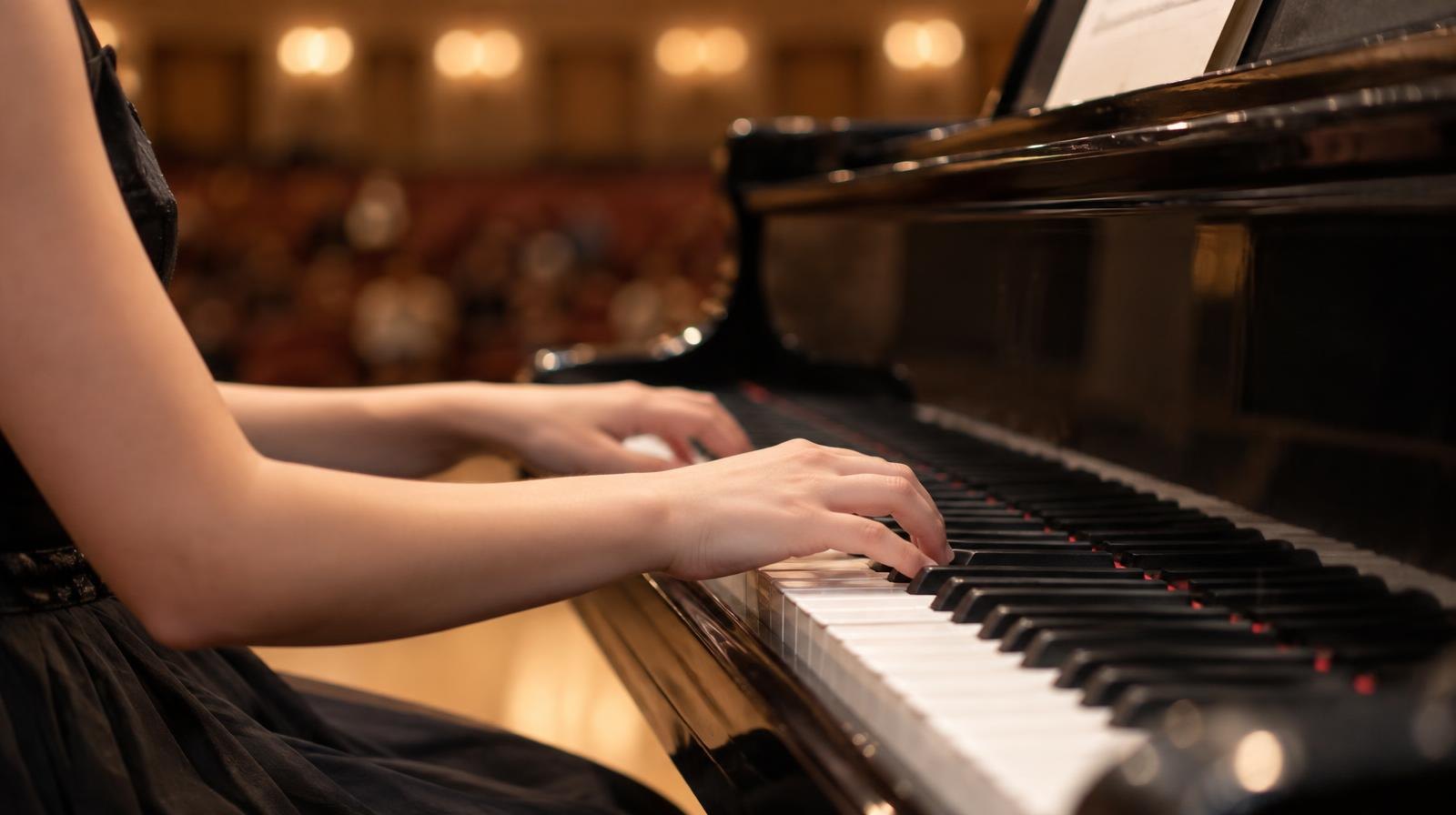 Close-up of hands resting on grand piano keys under warm stage lighting.