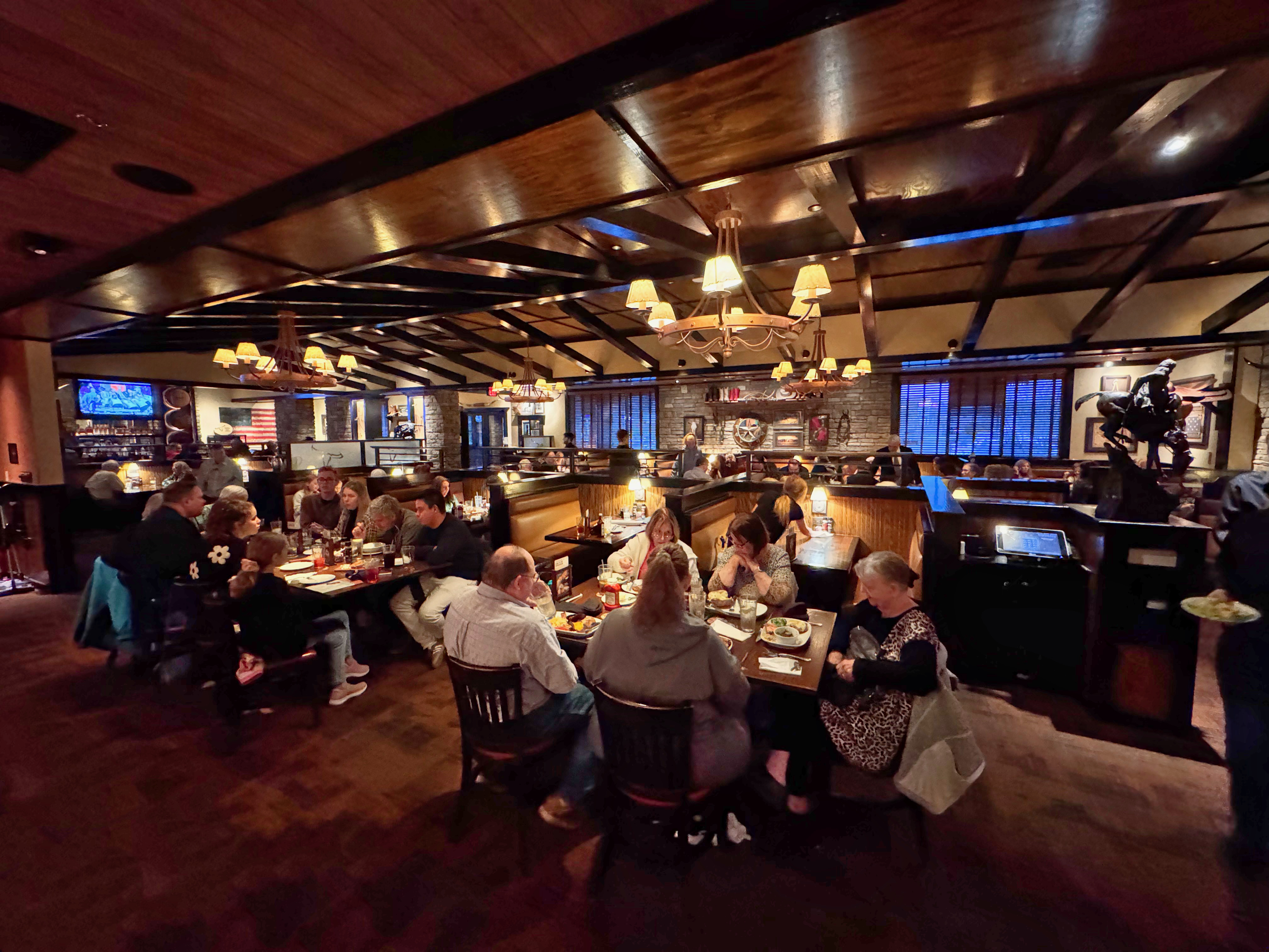 Busy steakhouse dining room with wood-beam ceiling and warm pendant lighting.