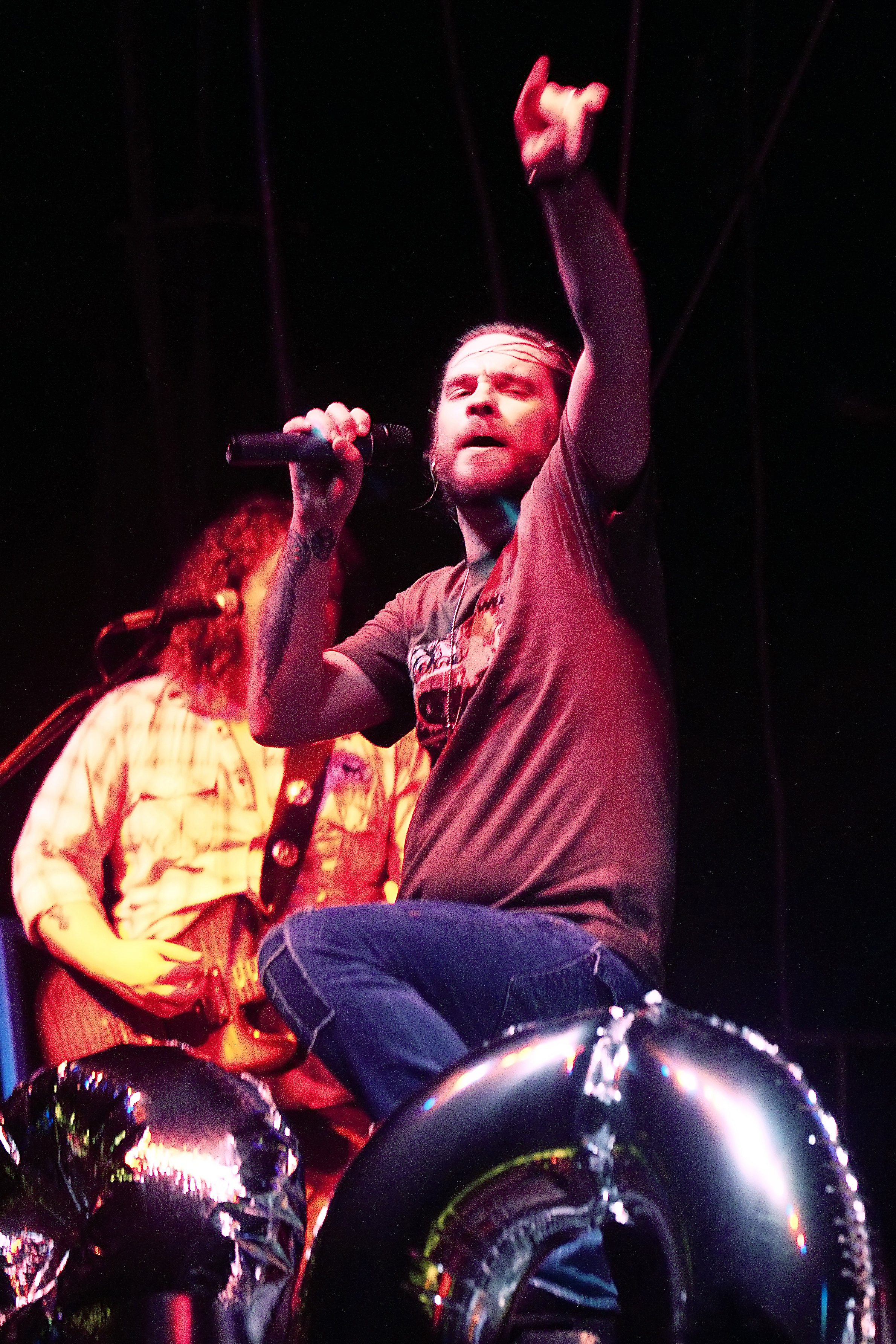 Male vocalist on stage holding a microphone with one arm raised, red stage lighting.