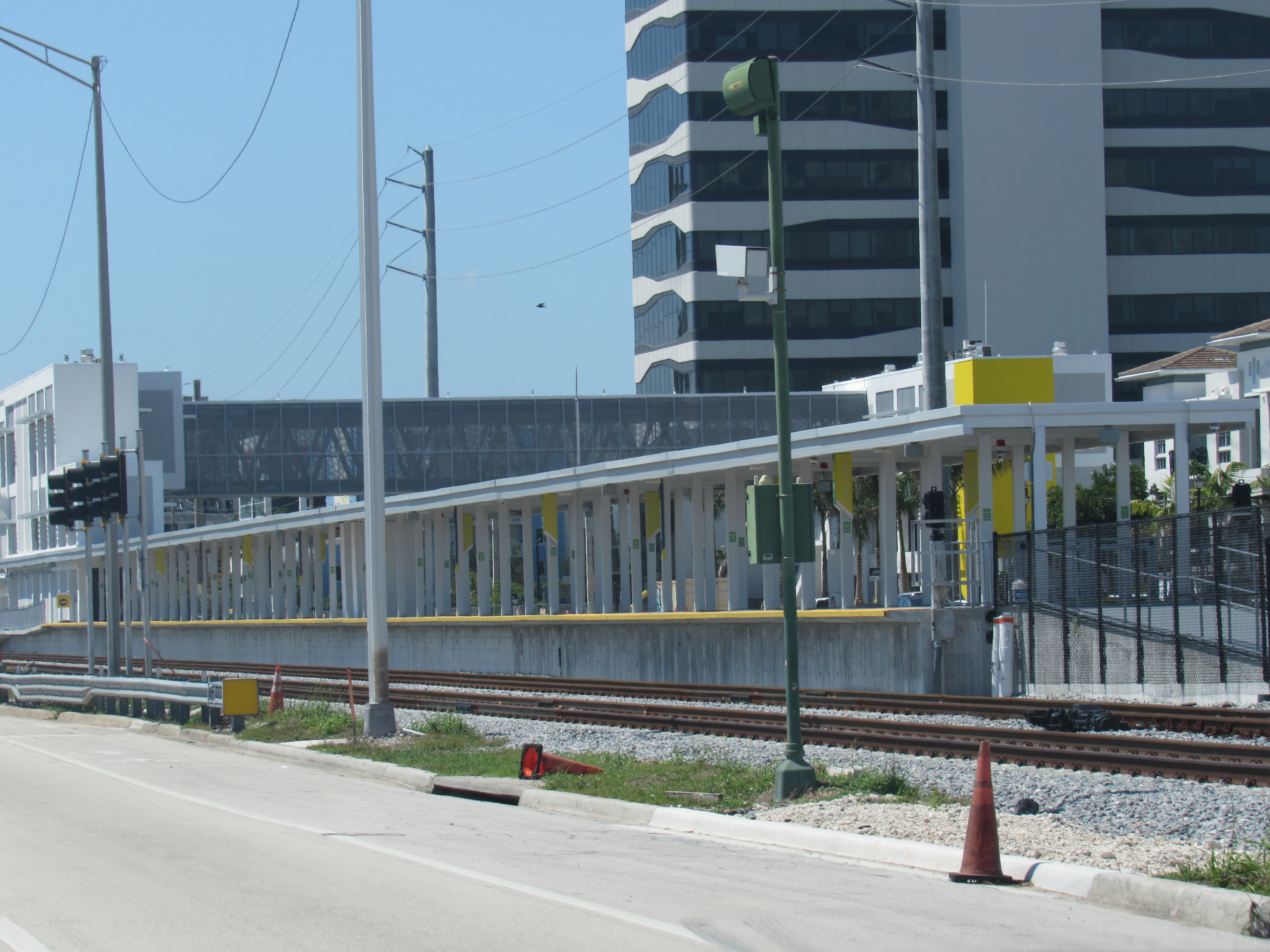 Train station platform with yellow safety railings, tracks in foreground, and tall building behind.