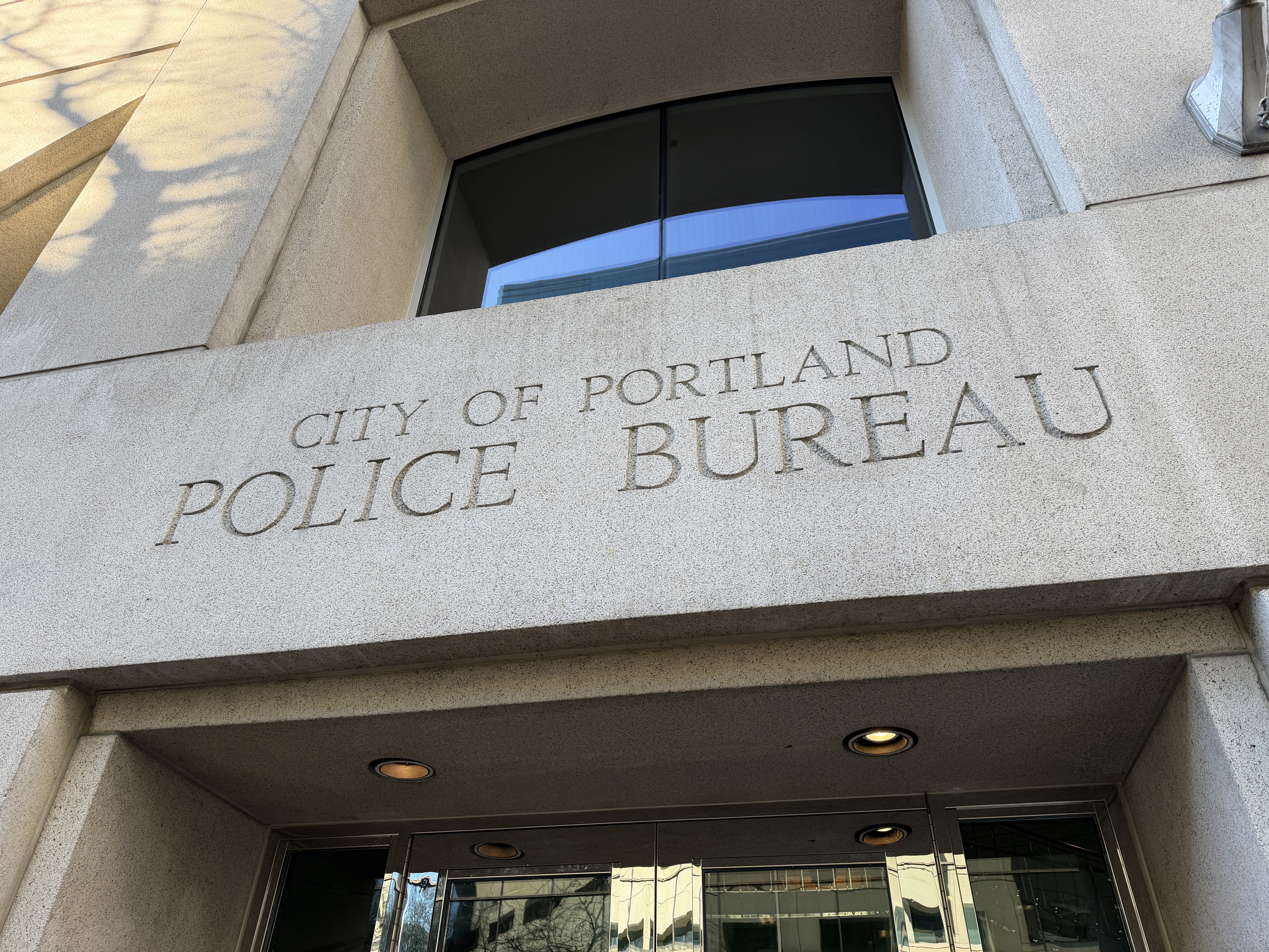 Stone building entrance with engraved 'City of Portland Police Bureau' inscription above glass doors.