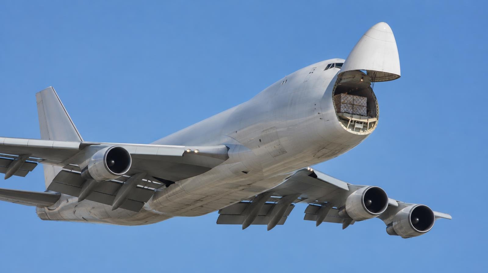 A large cargo aircraft flies against a clear blue sky viewed from below.