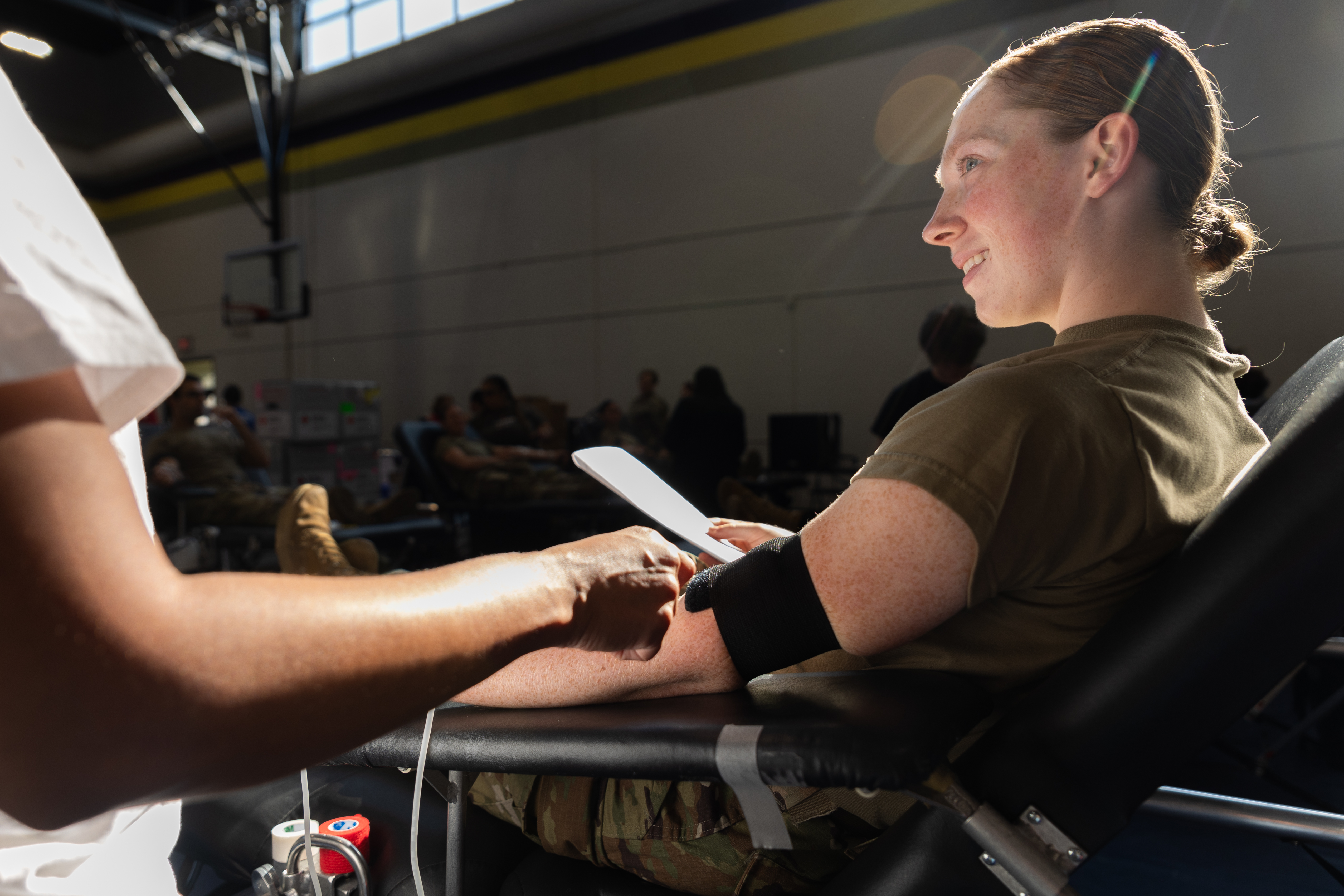A smiling woman in a green shirt has her arm prepared for a blood draw at a donation center.